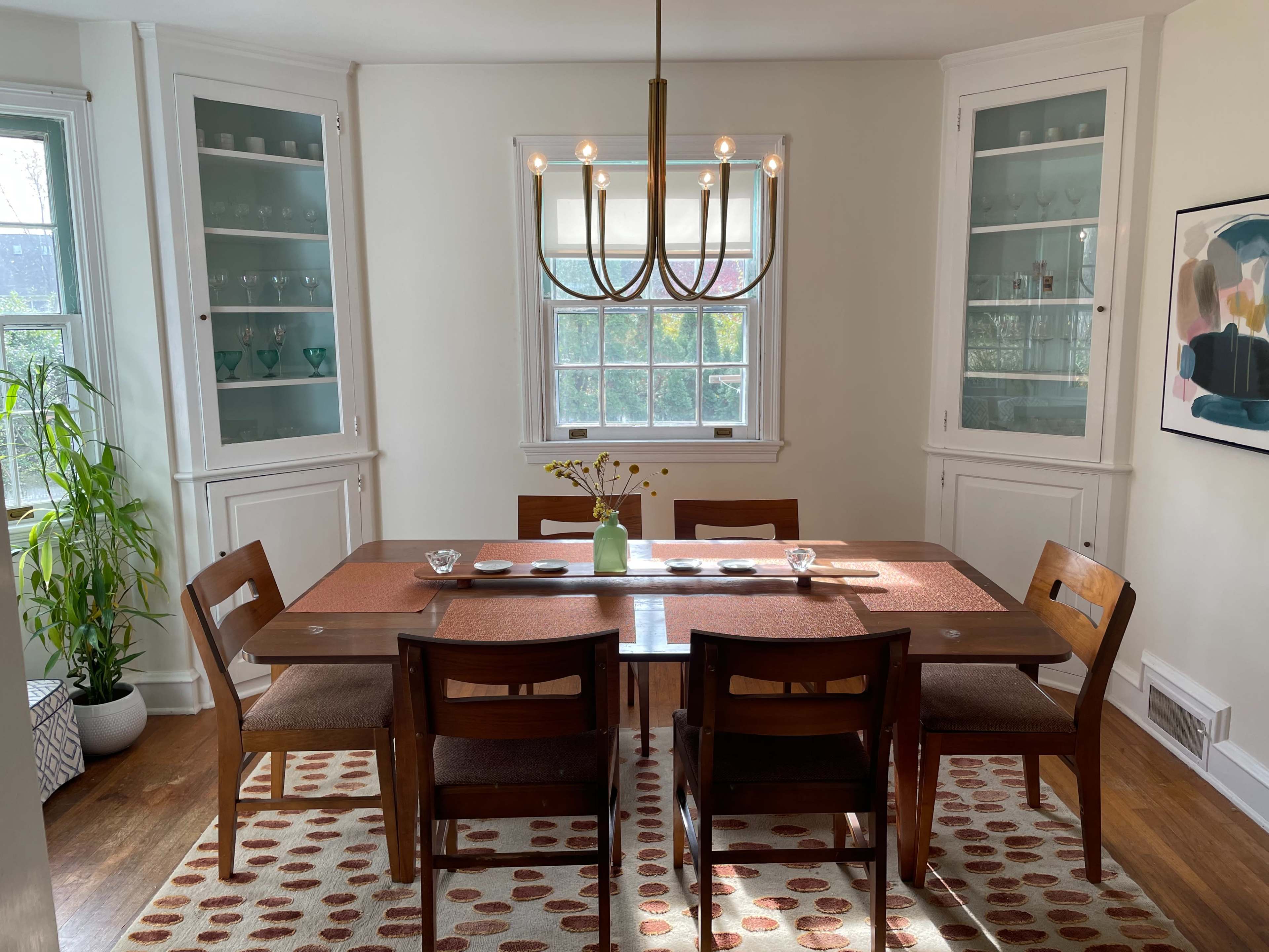 A dining room features a wooden table with chairs, surrounded by lighted cabinets and a decorative rug.