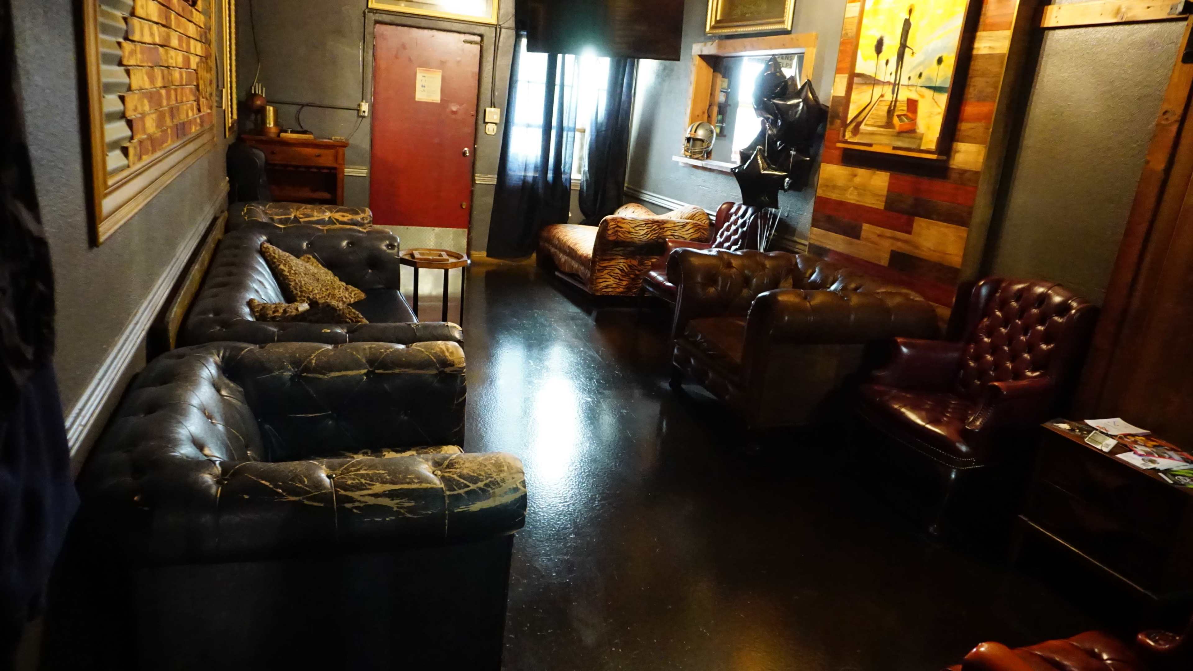 The image shows a cozy waiting area with various leather couches, a wooden door, and framed artwork on the walls.