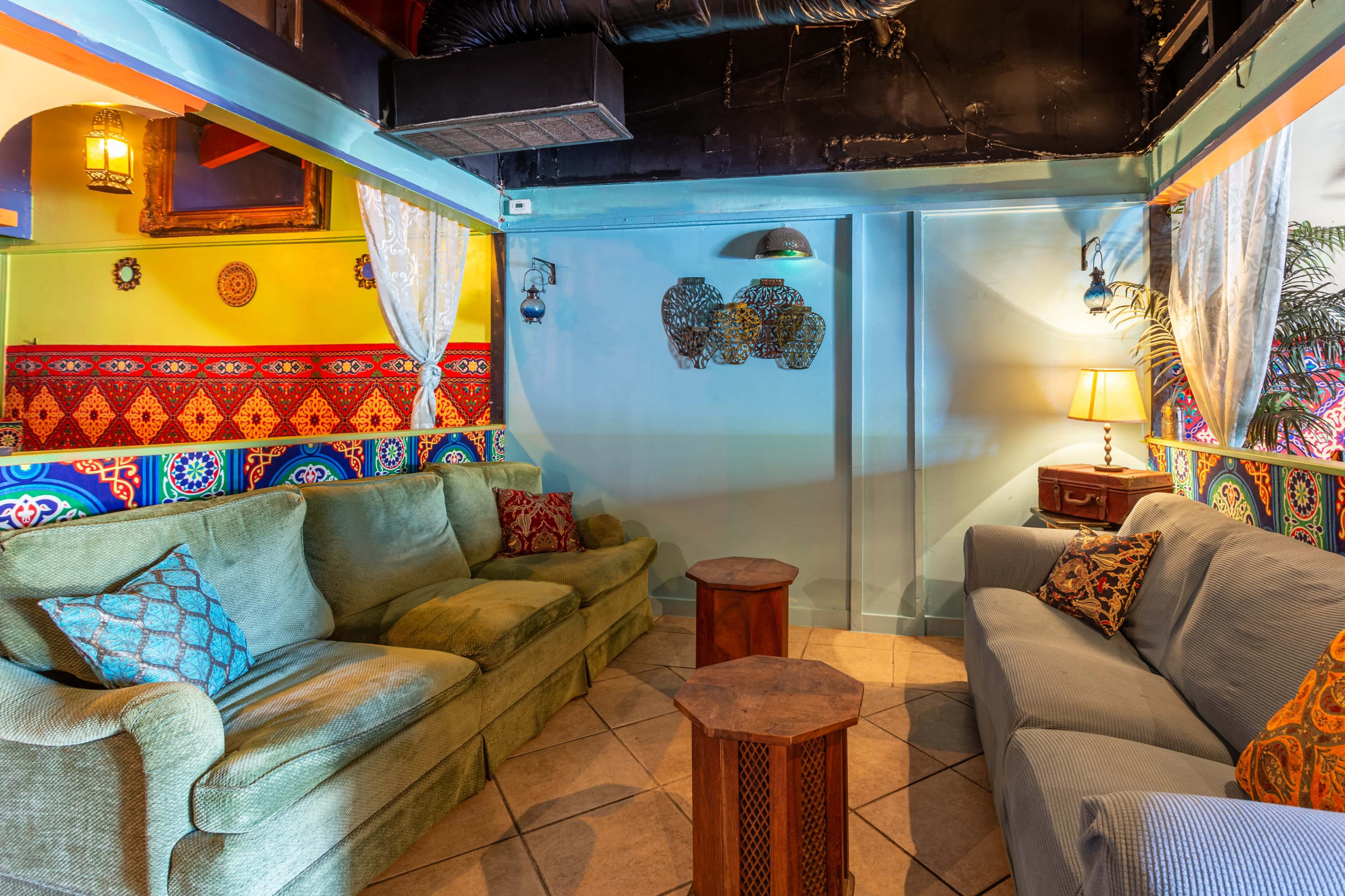 A cozy seating area with two sofas and wooden tables, adorned with decorative pillows, against brightly colored walls.