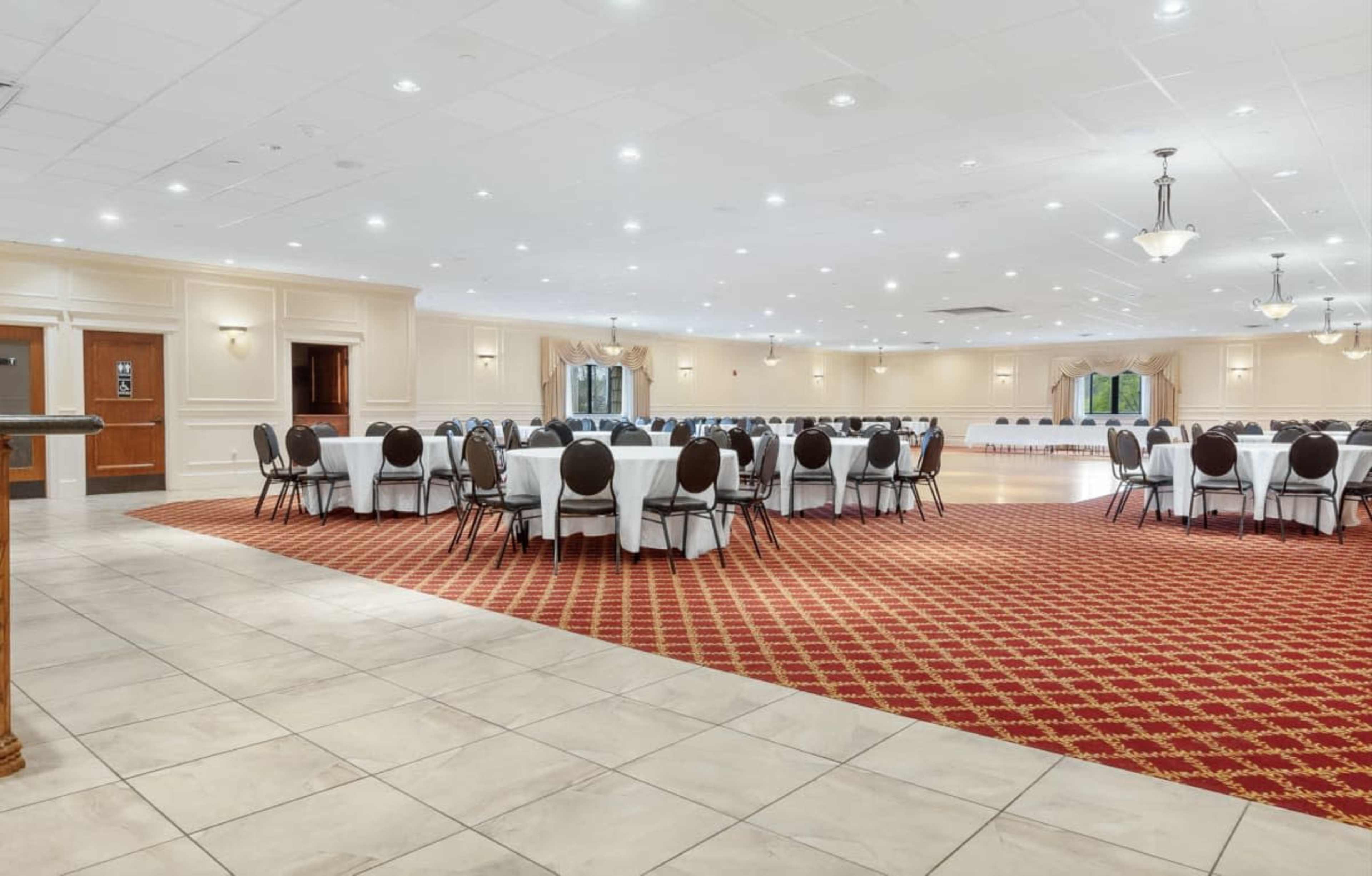 The image shows a spacious event hall with several round tables and chairs arranged in a carpeted area.