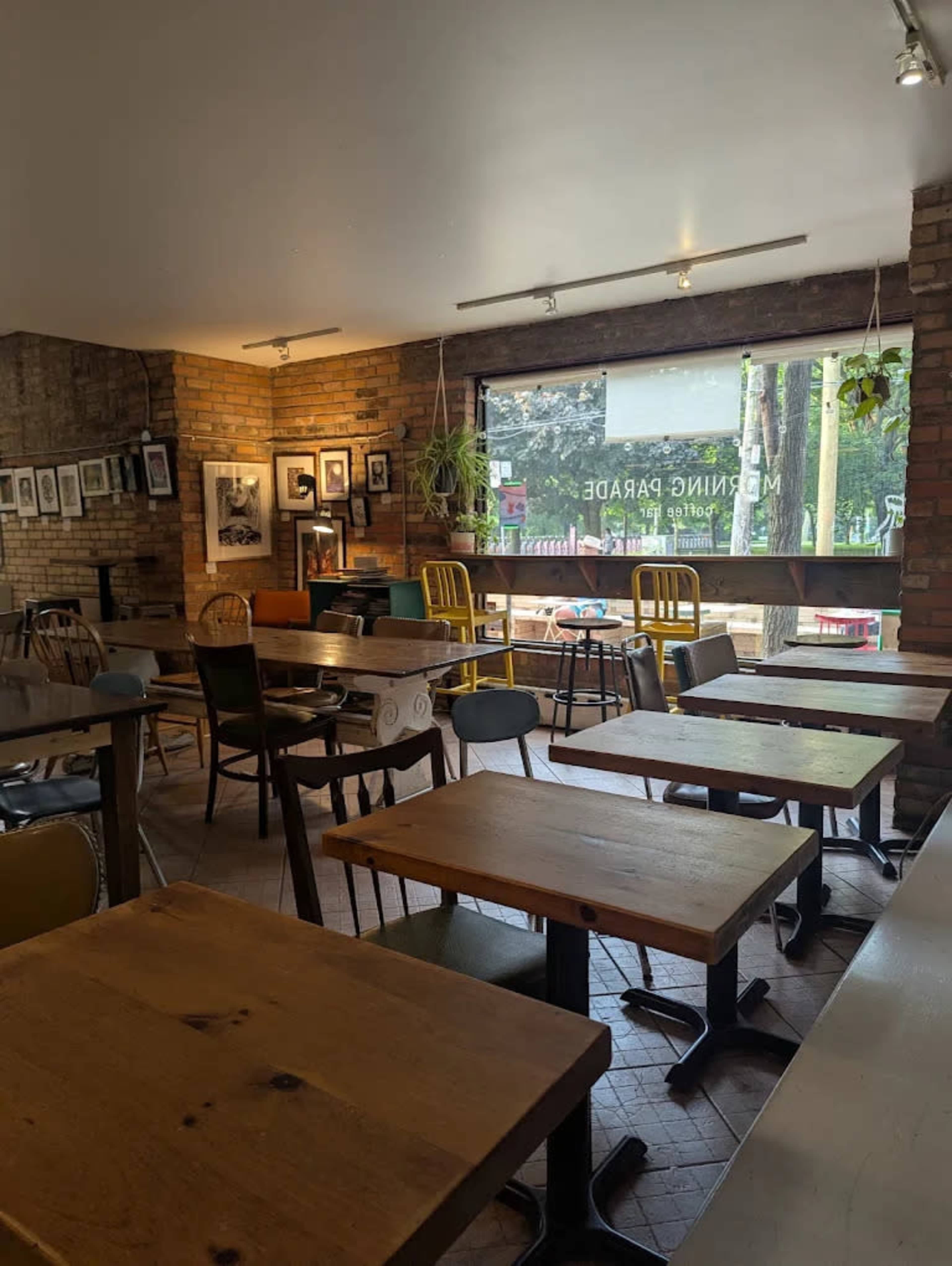The image shows an indoor café space with various tables and chairs arranged, brick walls, and large windows letting in natural light.