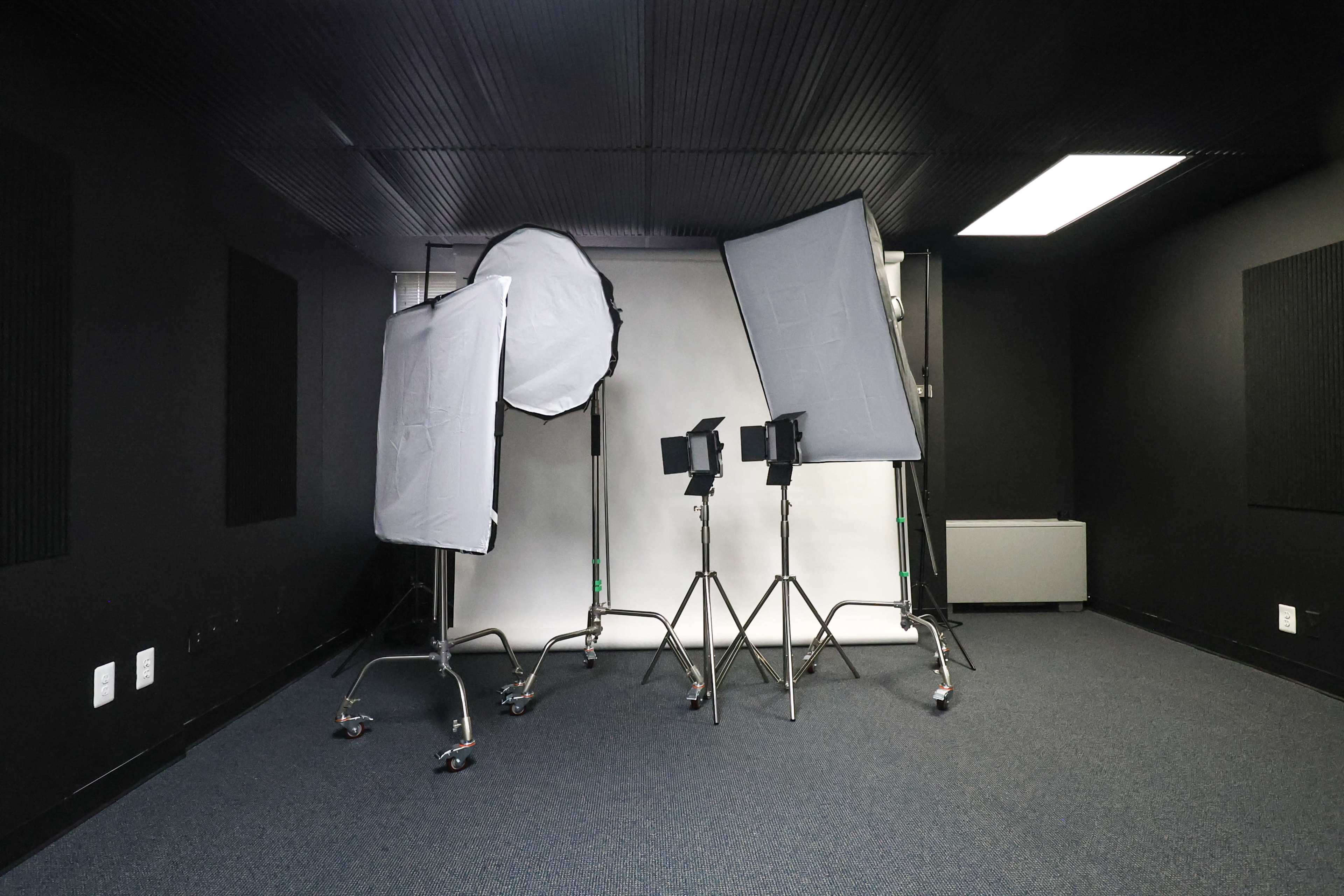 The image depicts a studio space featuring multiple light setups and a white backdrop on a dark floor.