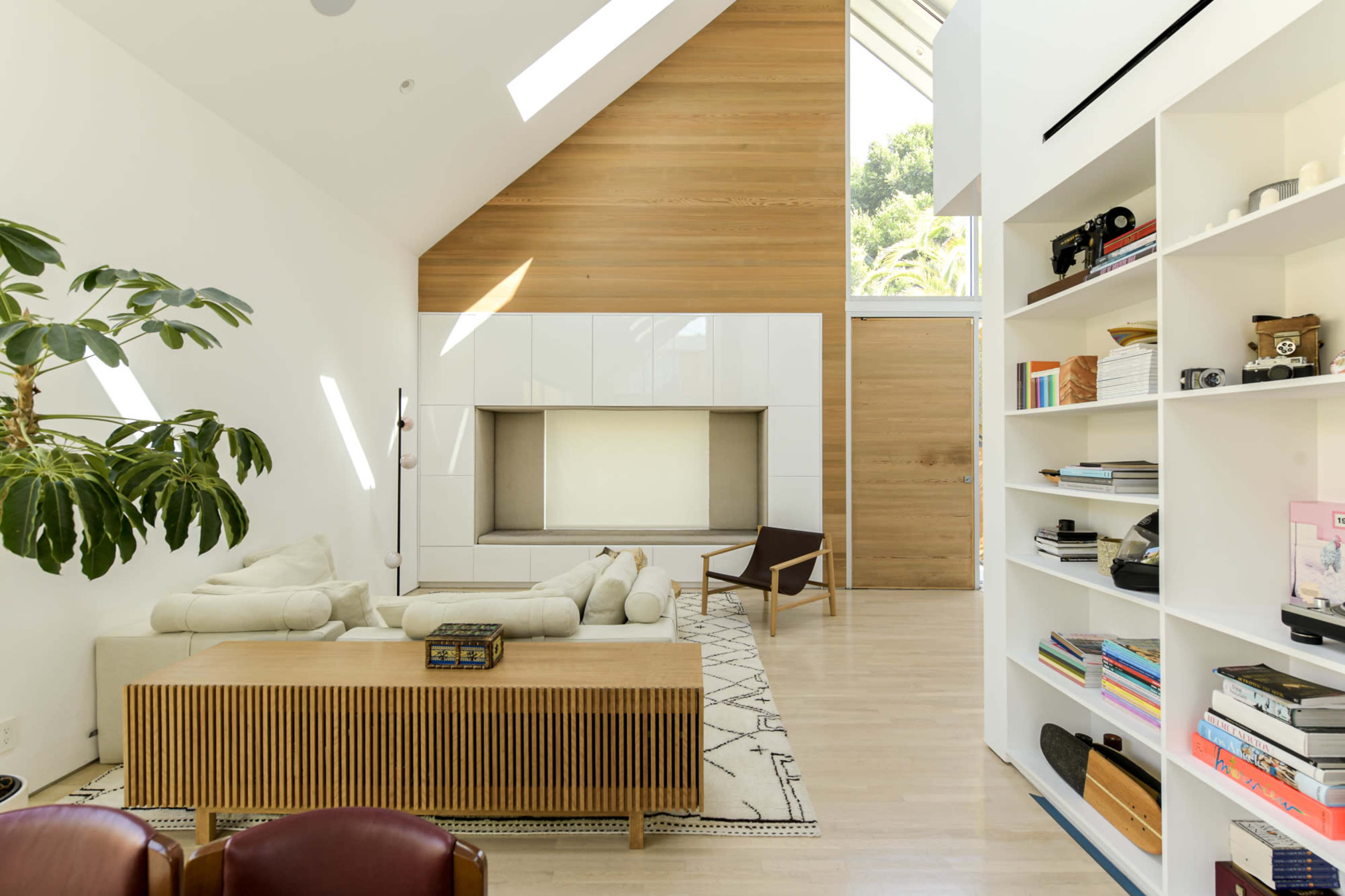 A spacious living room features a large white sectional sofa, a wooden coffee table, and shelves filled with books and decorative items.