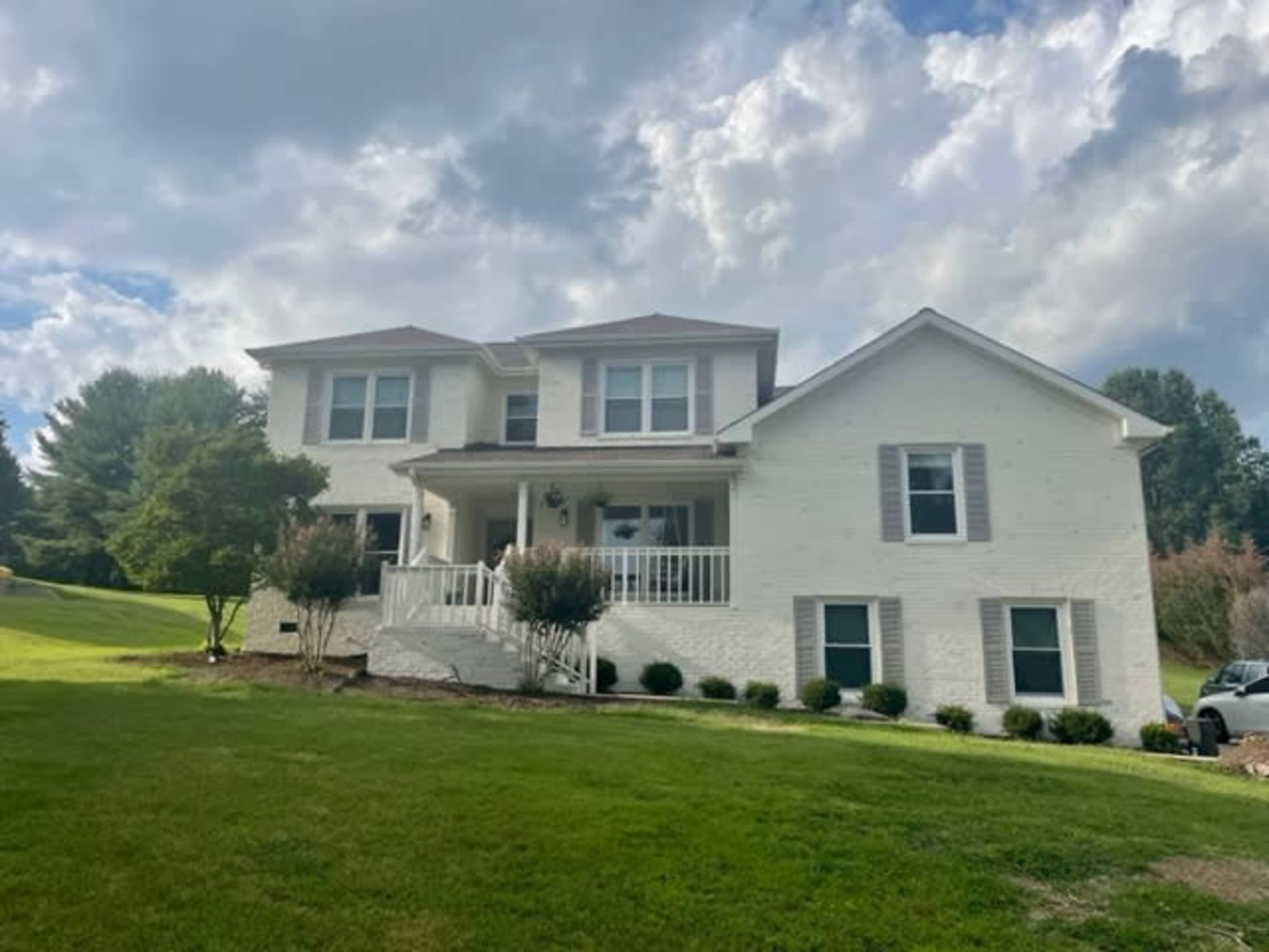 A two-story white brick house with a covered front porch and landscaped lawn.