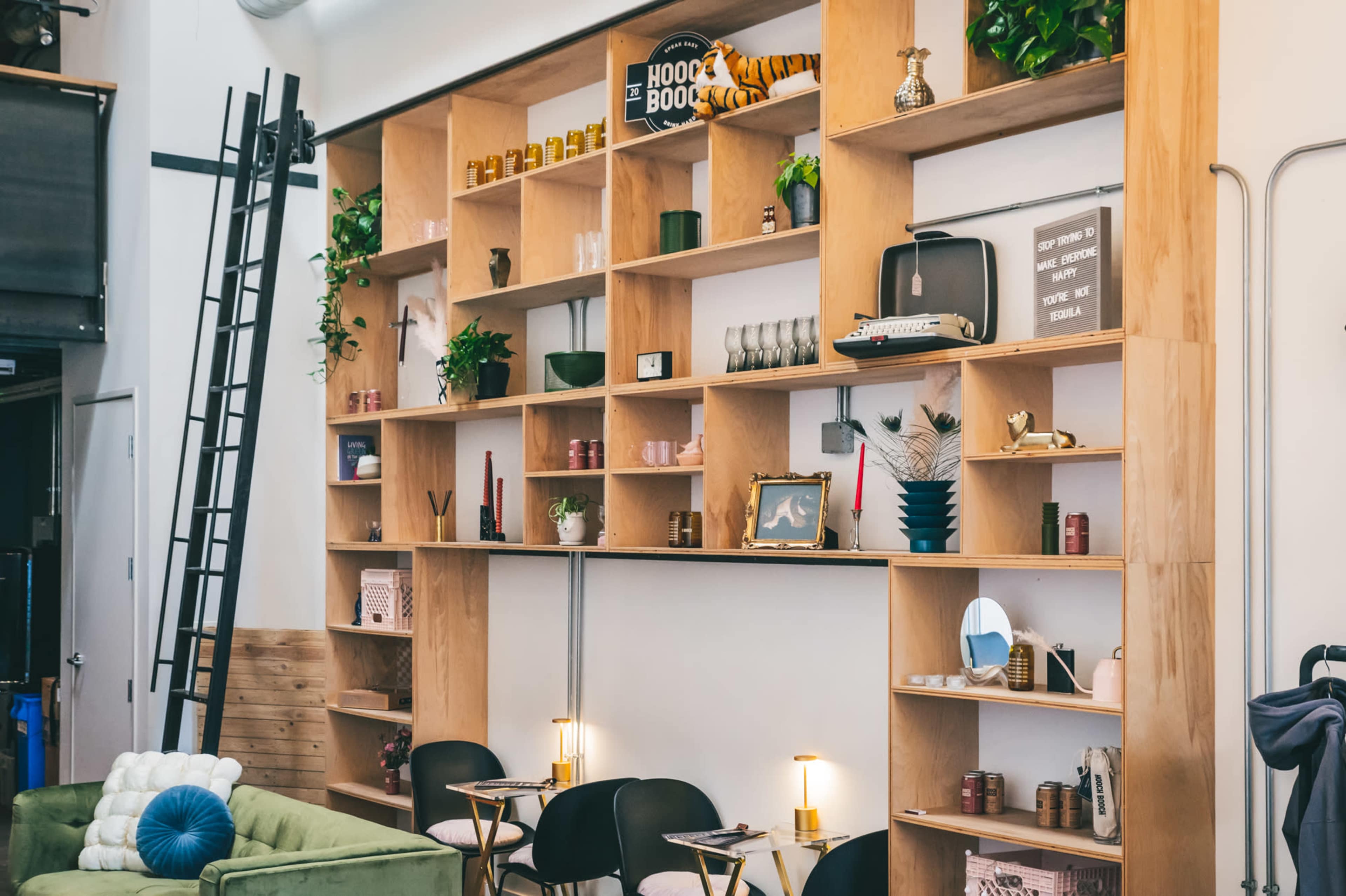 A wooden shelving unit filled with various decorative items, including plants, candles, and books, alongside seating arranged in front of it.