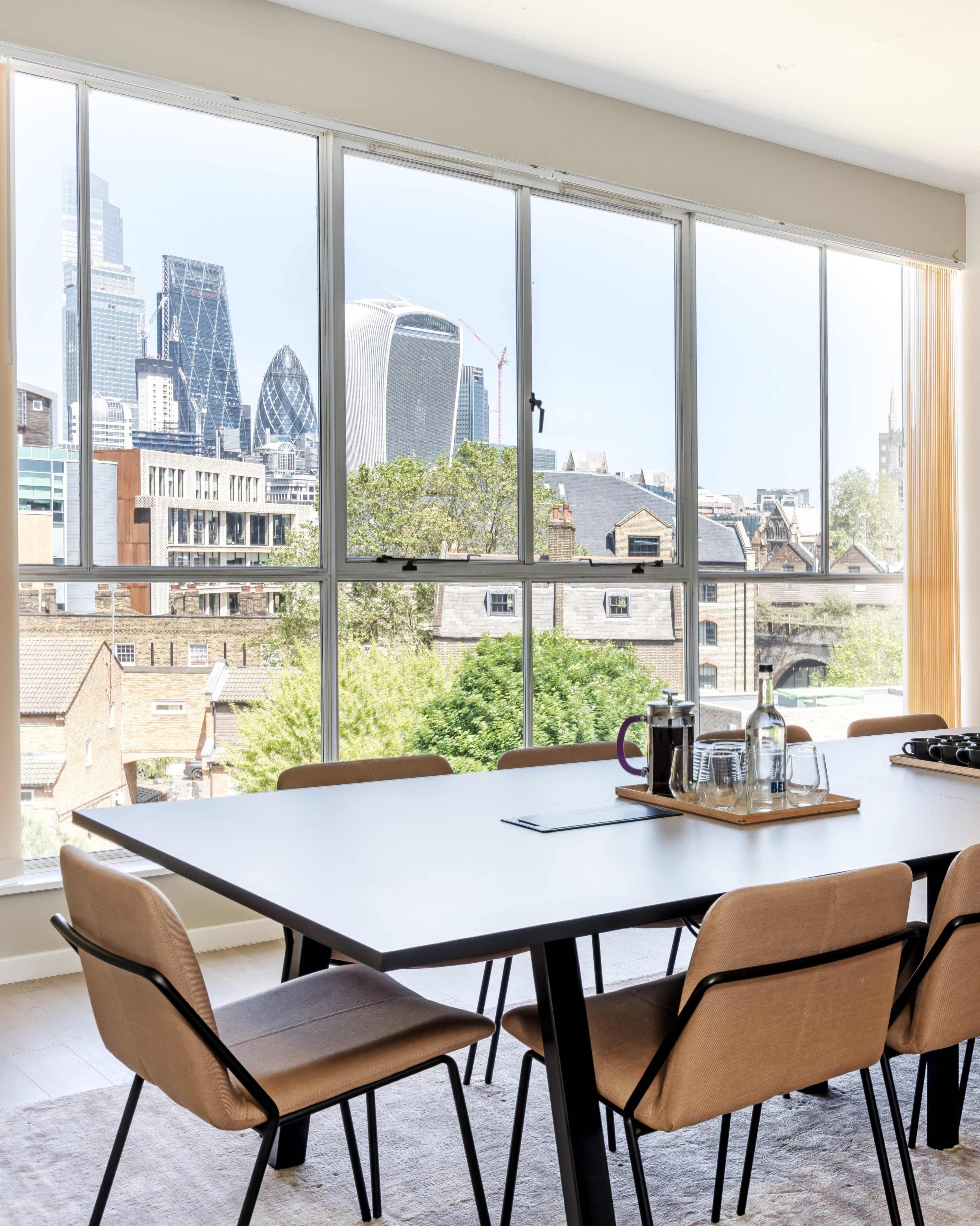 A modern dining area features a large table set with a tray of drinks, overlooking a city skyline through large windows.