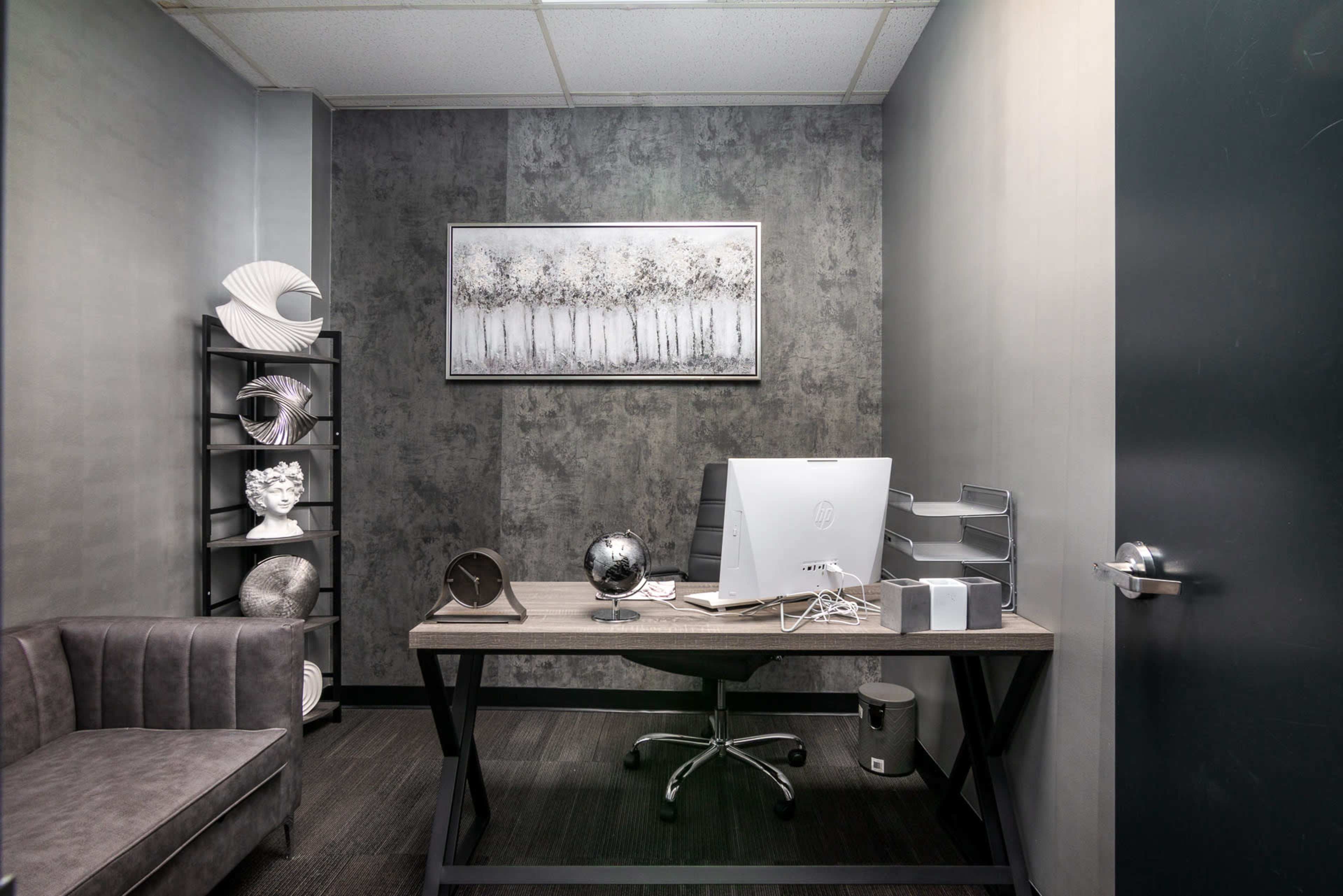 A modern office with a desk, a computer, decorative sculptures on shelves, and a gray sofa along one wall.