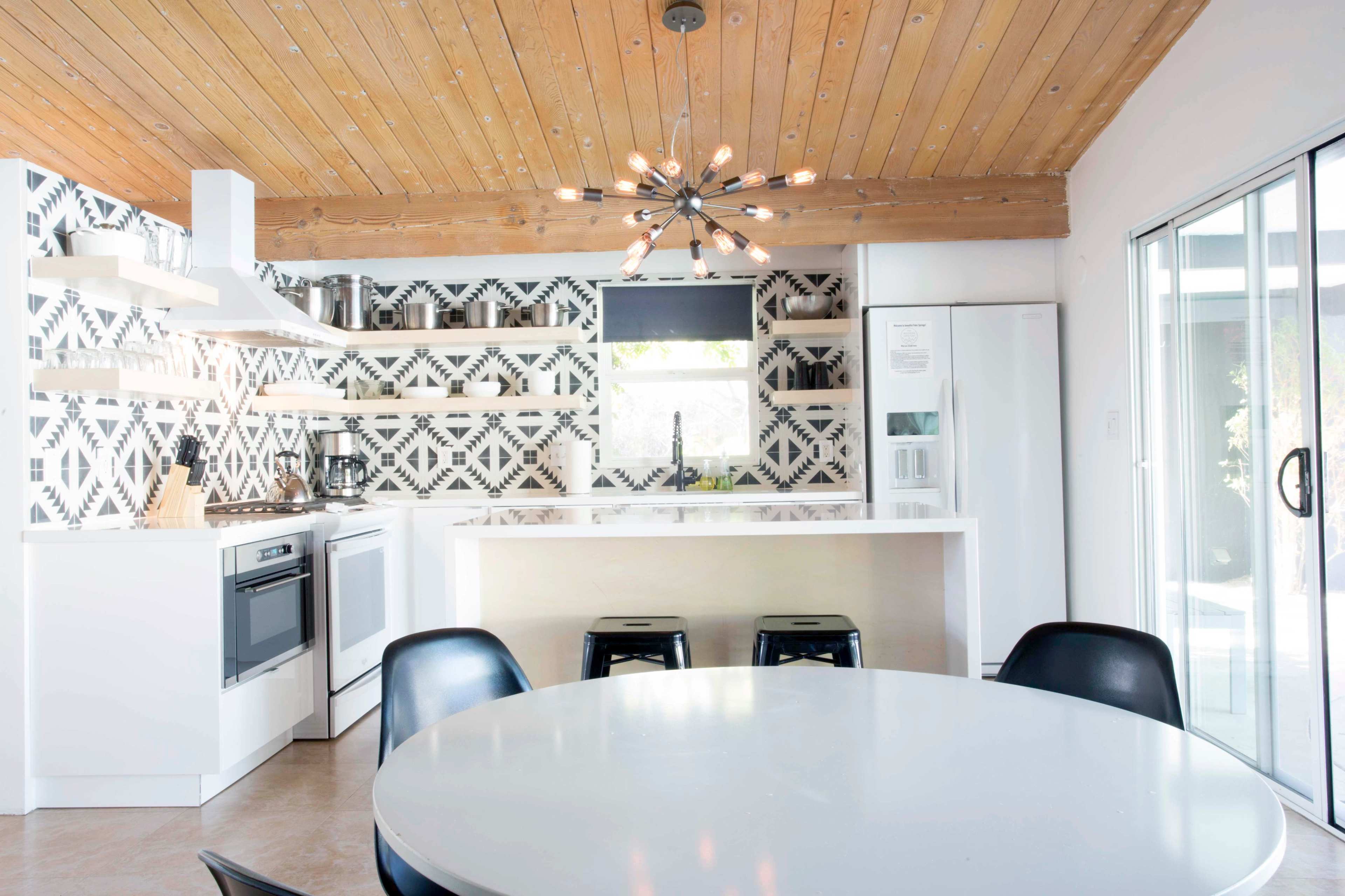 A modern kitchen with a geometric-patterned backsplash, a white countertop, and a round dining table with black chairs.