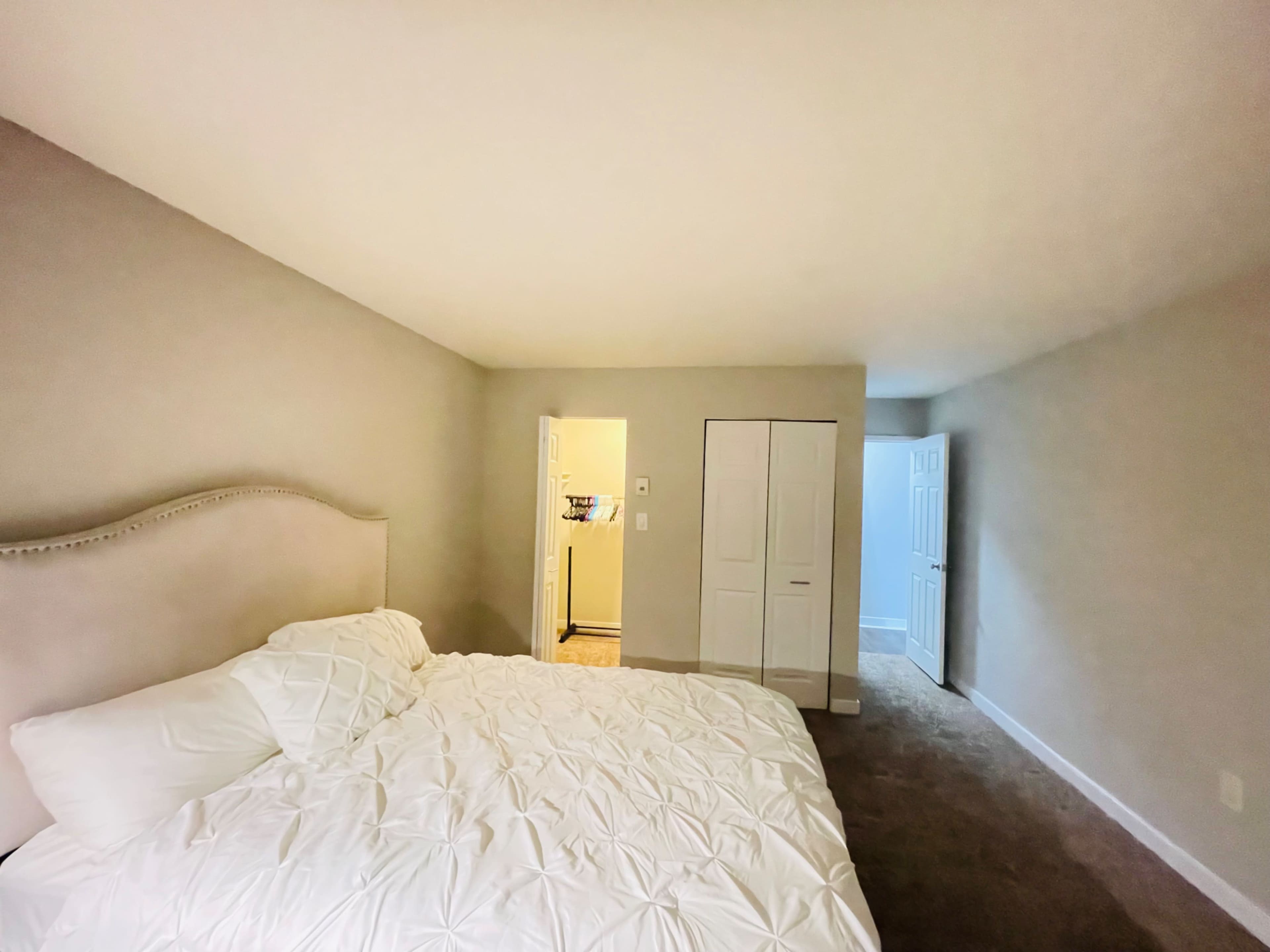 A simple bedroom with a large bed, a closet, and a doorway leading to another room.
