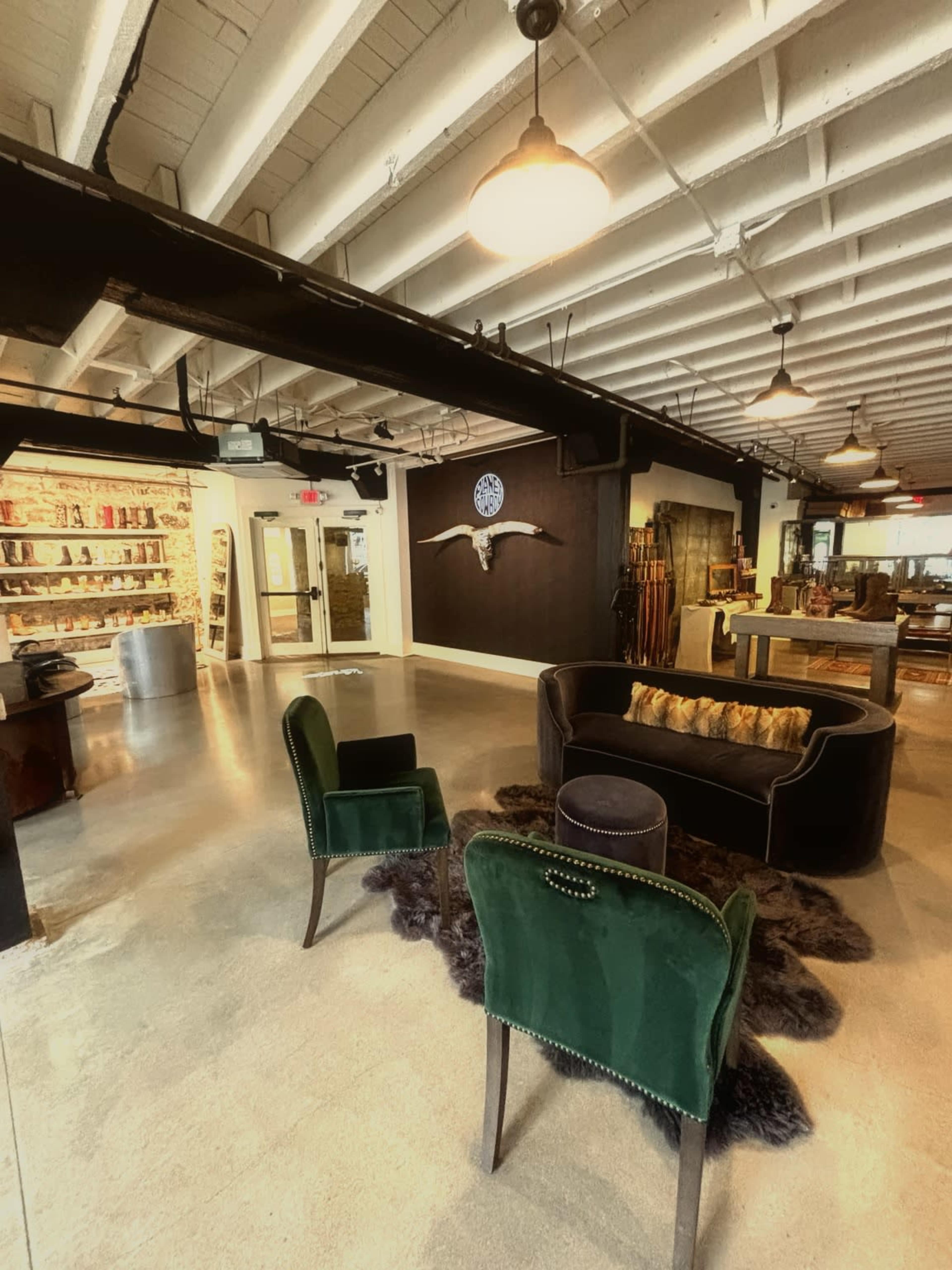 The image shows a modern interior space featuring two green upholstered chairs, a dark velvet sofa, a decorative wall clock, and a variety of items displayed on shelves.
