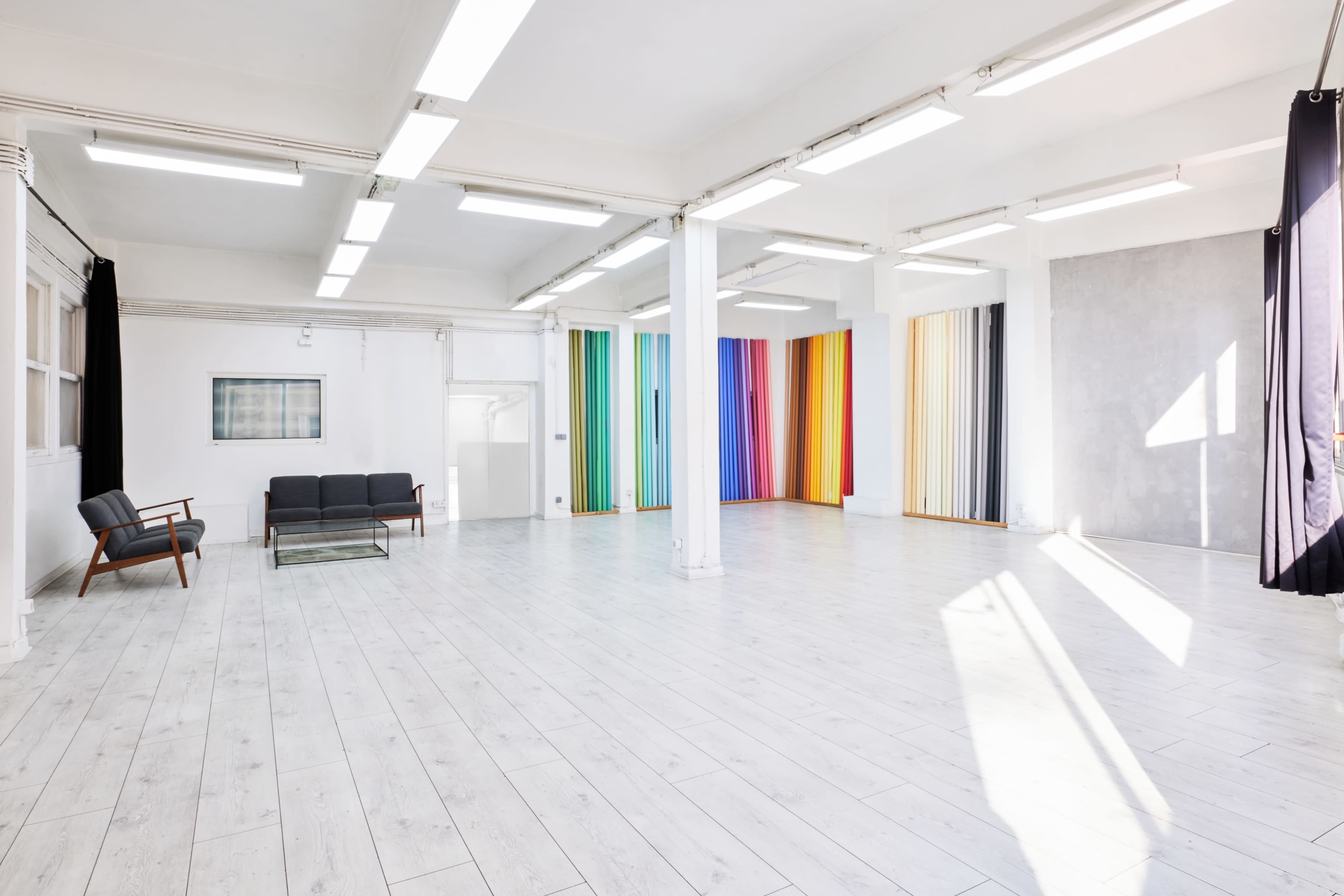 The spacious interior features a light-colored wooden floor, a black seating area, and vibrant vertical stripes of color on the walls.