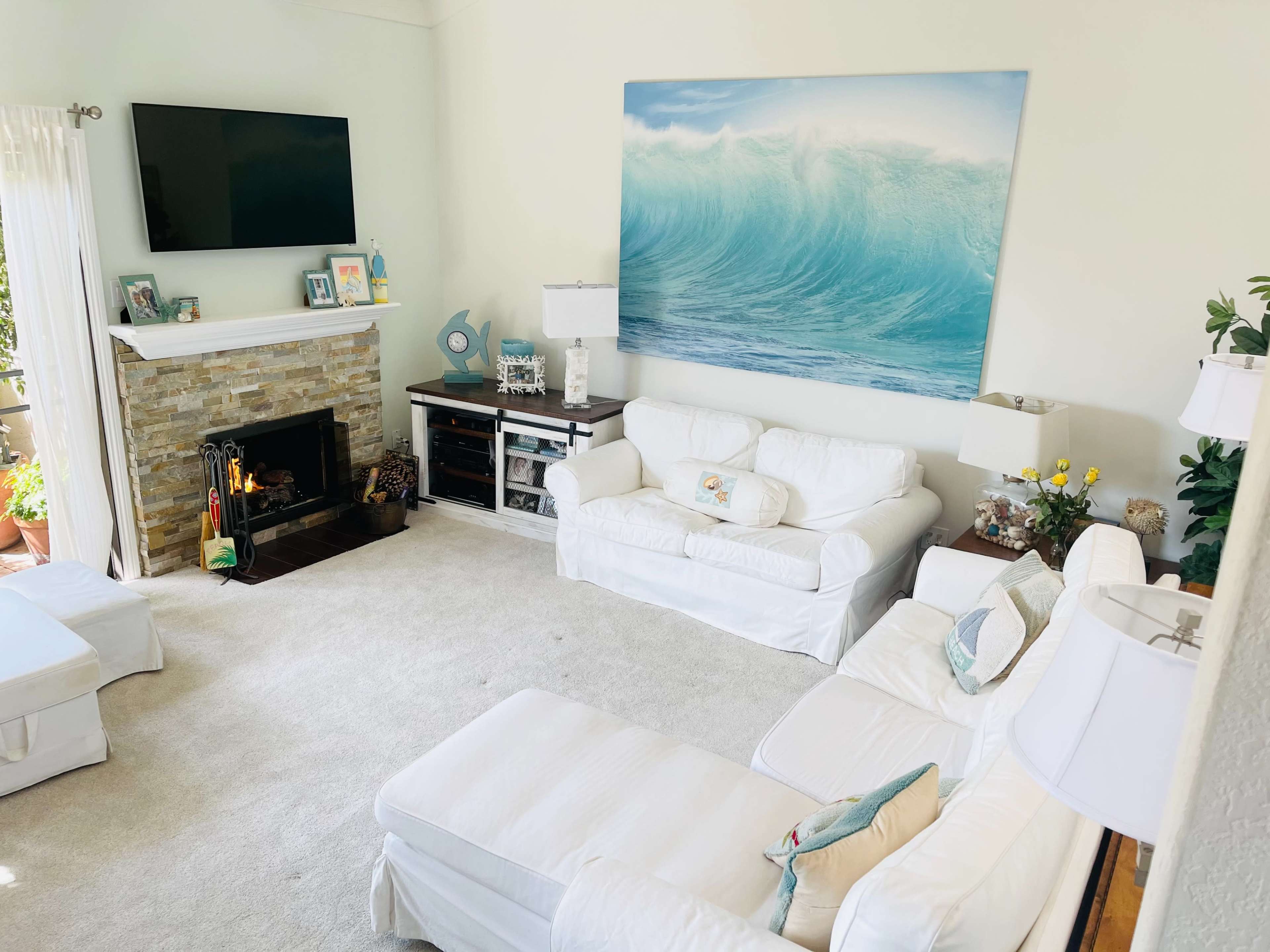 The living room features white furniture, a stone fireplace, and a large wave painting above the mantel.