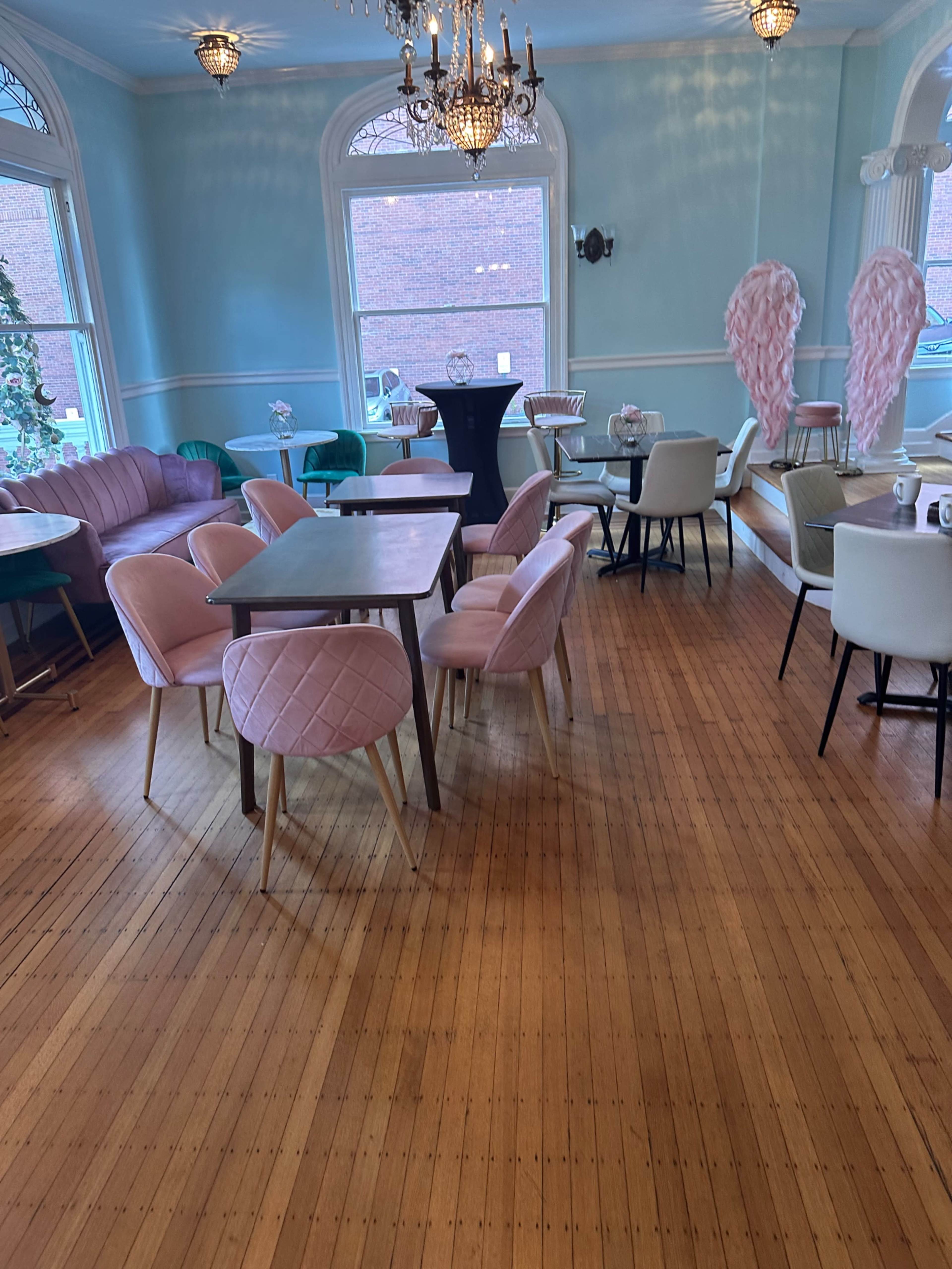 A brightly lit café with various seating arrangements, including tables and chairs in pastel colors, and large windows providing natural light.