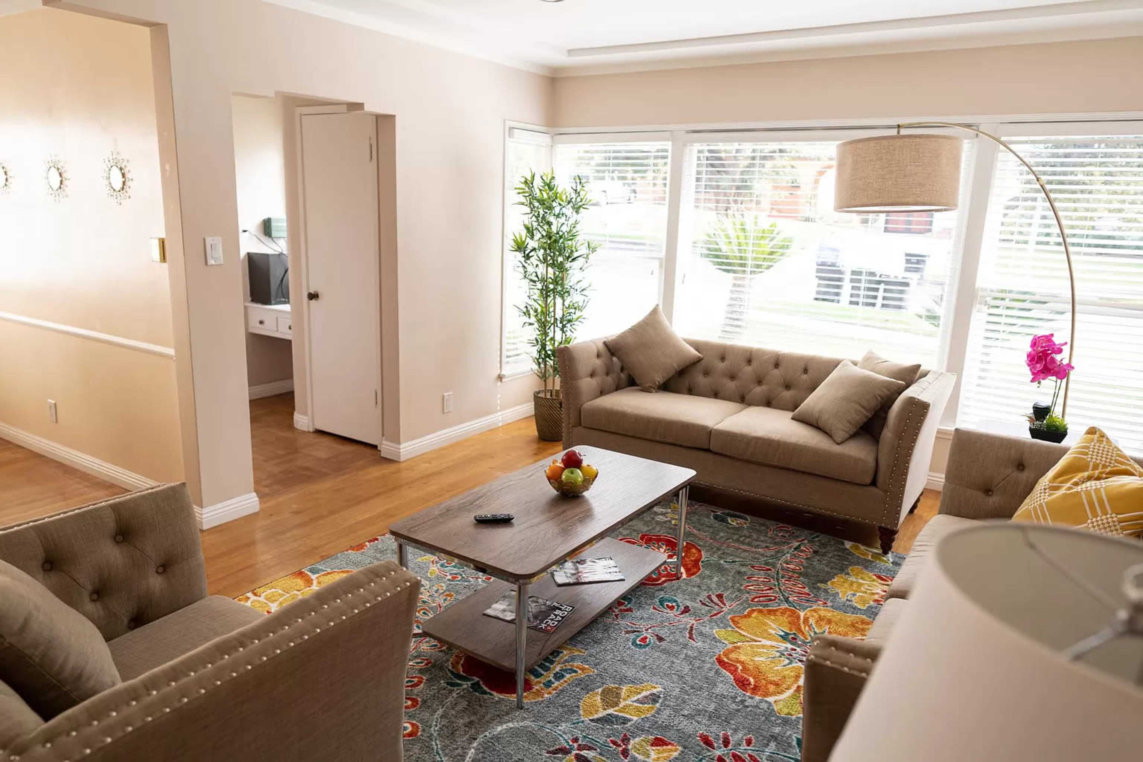 A well-lit living room features two sofas, a coffee table with decorative items, and large windows allowing daylight to enter.