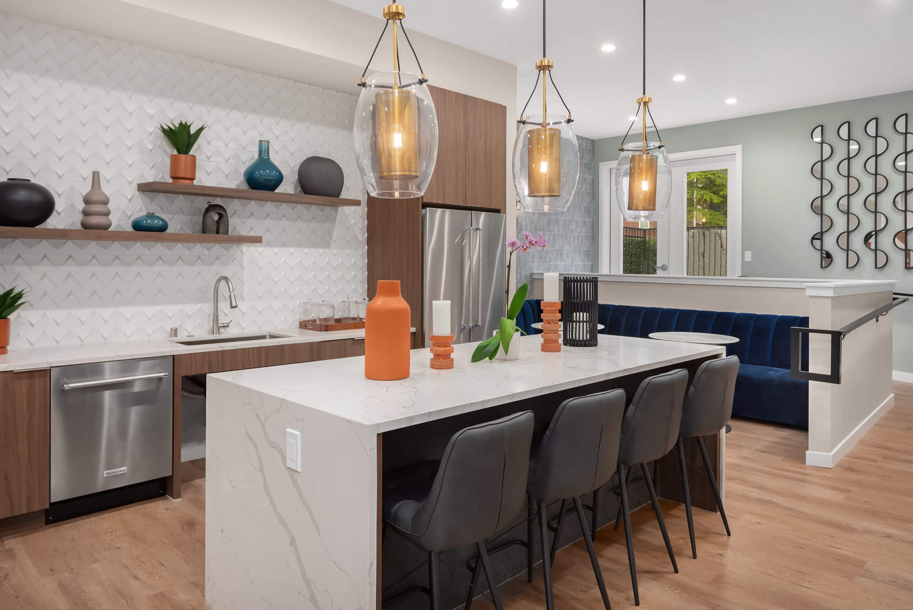 A modern kitchen with a large island, featuring pendant lights, bar stools, and a mix of wooden and white cabinetry against a textured backsplash.