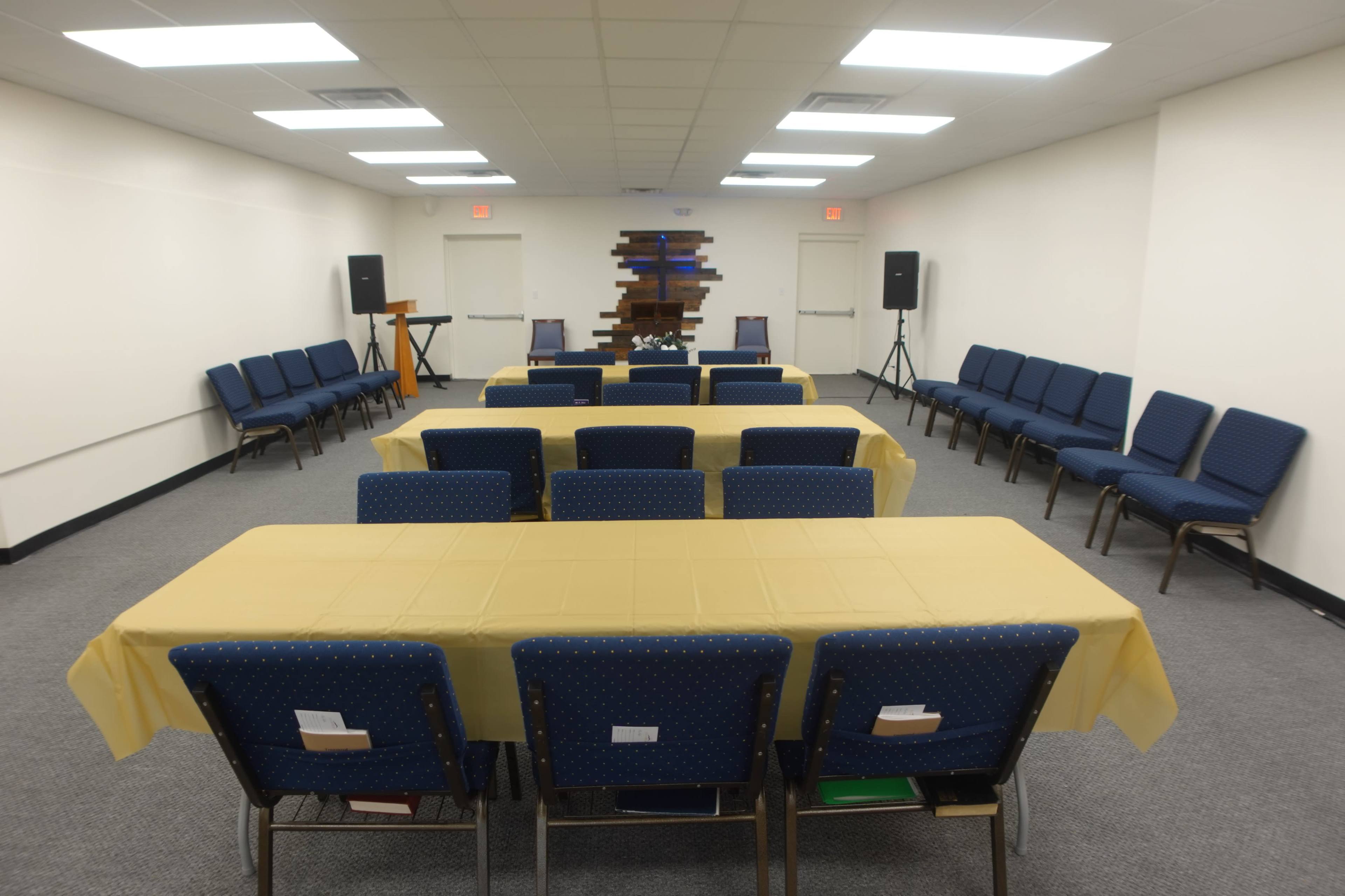 A meeting room is set up with two rows of blue chairs and several tables covered with yellow tablecloths.