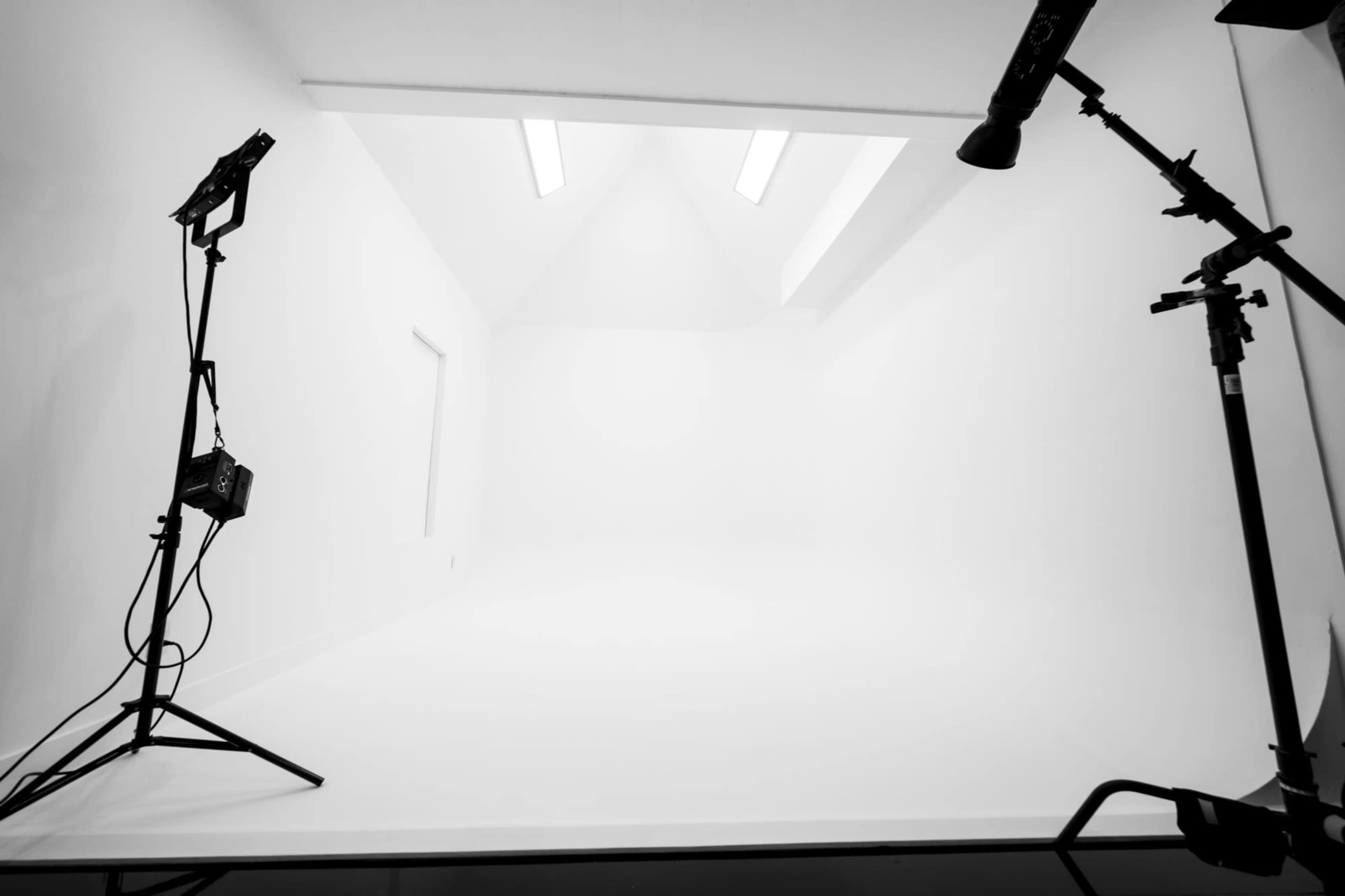A minimalistic photography studio with white walls and a stark empty space, illuminated by overhead lights.