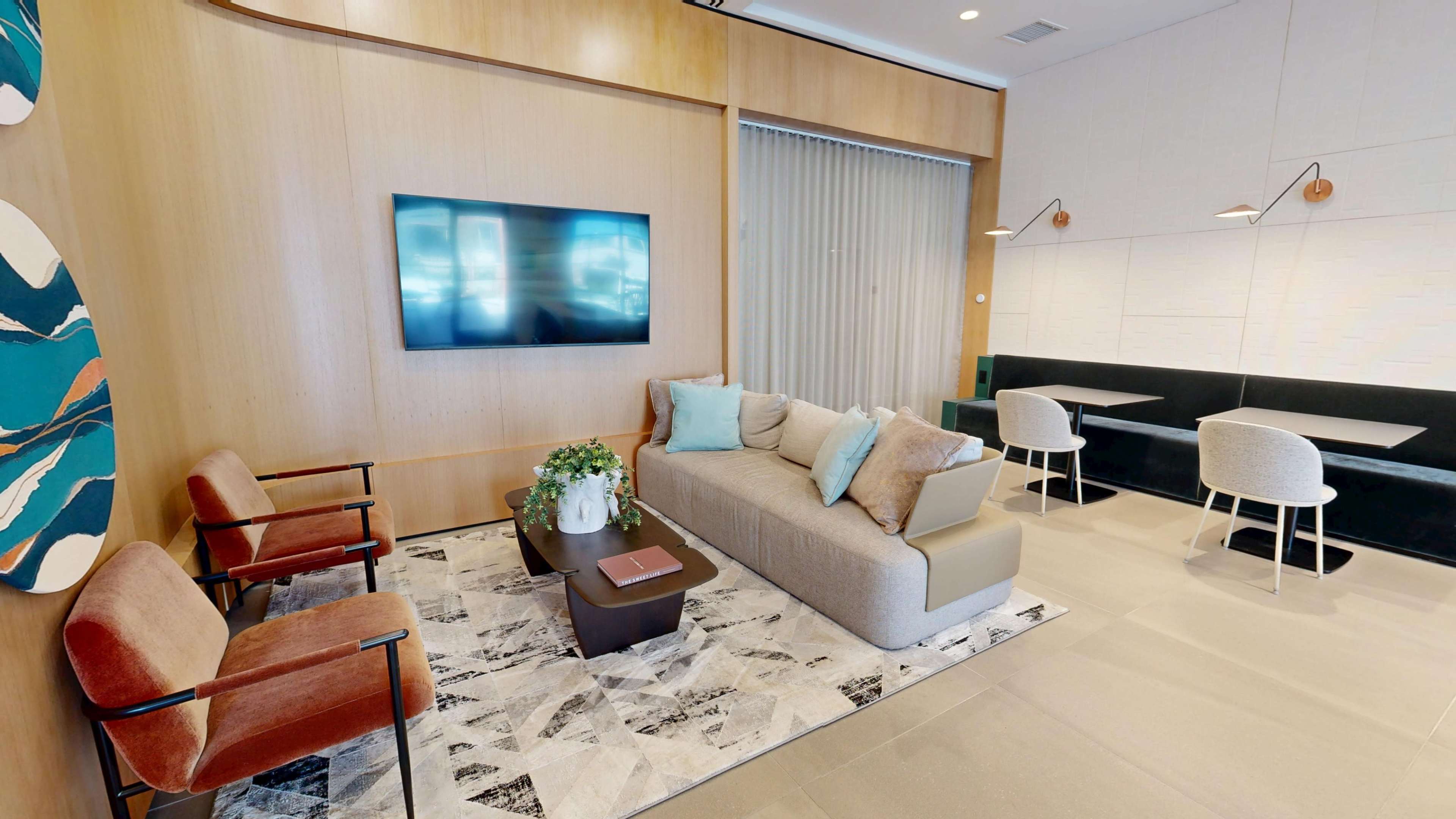 The image shows a modern lounge area with a sofa, two armchairs, a coffee table, and a wall-mounted television, all arranged on a patterned rug with a backdrop of wooden paneling.