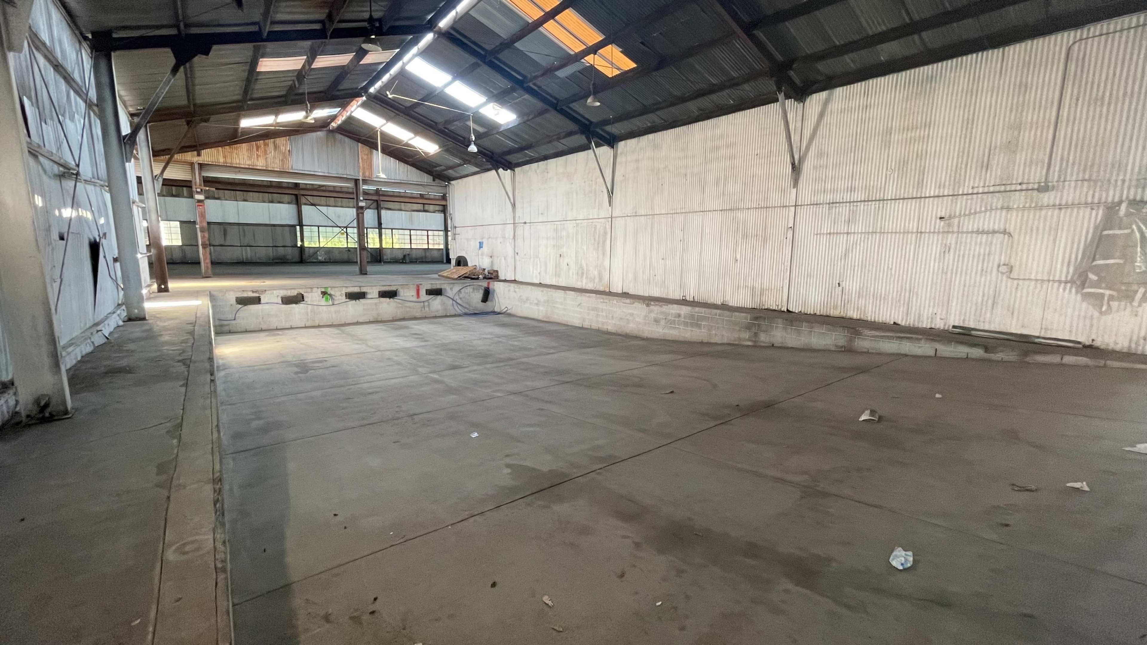 An empty industrial warehouse with concrete flooring and corrugated metal walls.