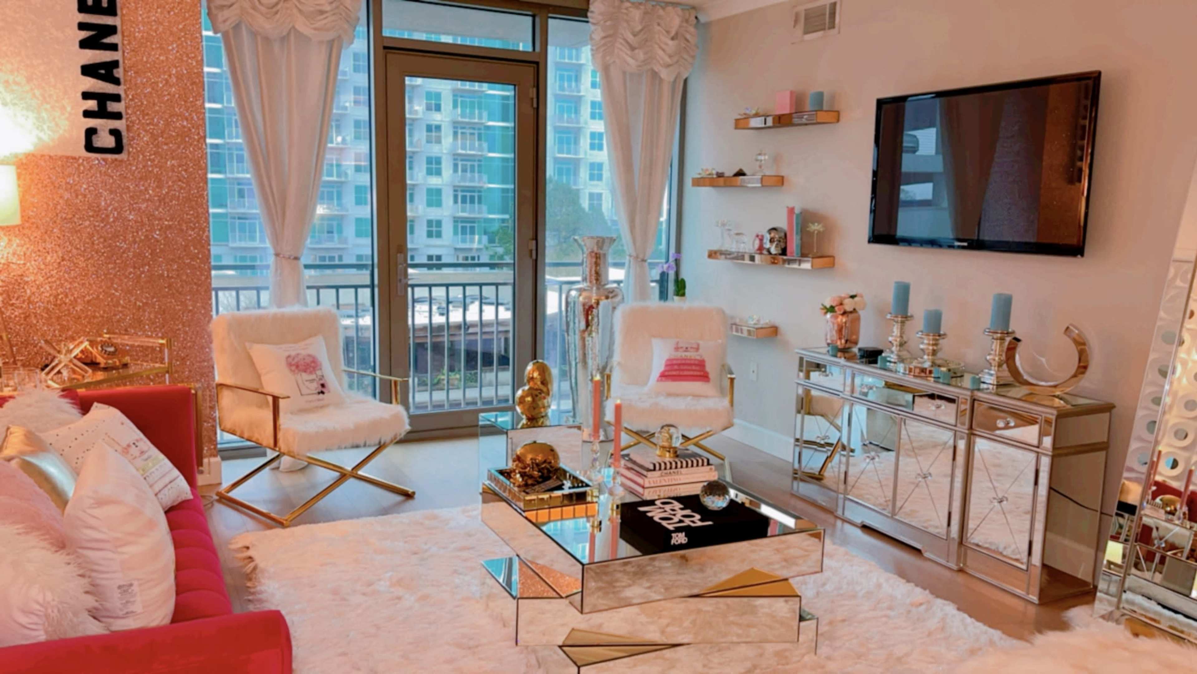 The living room features modern furniture with a plush white rug, a glass coffee table, and large windows that overlook a balcony.