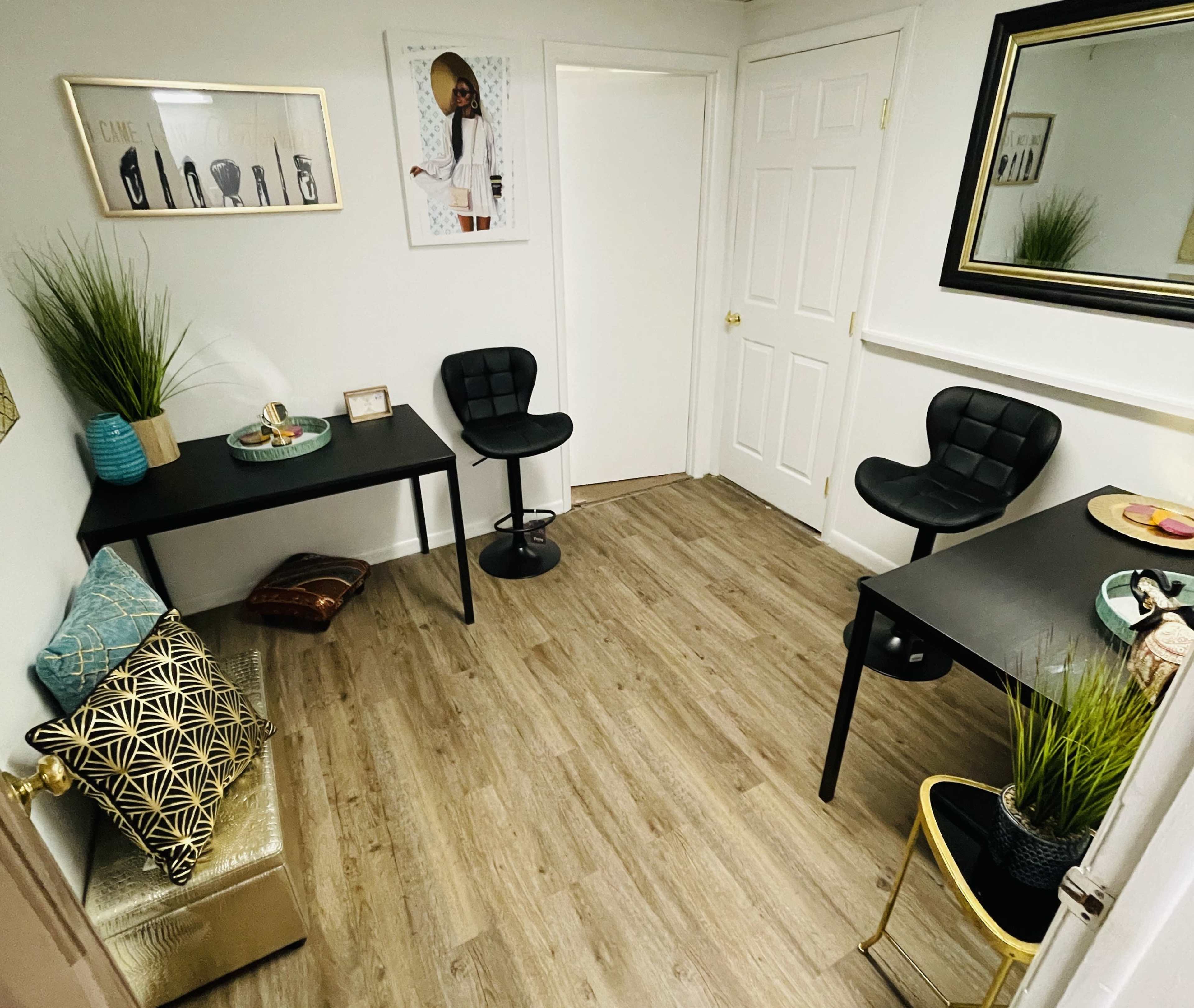 The image shows a small room with two black tables, two black stools, decorative plants, and a wall adorned with art.