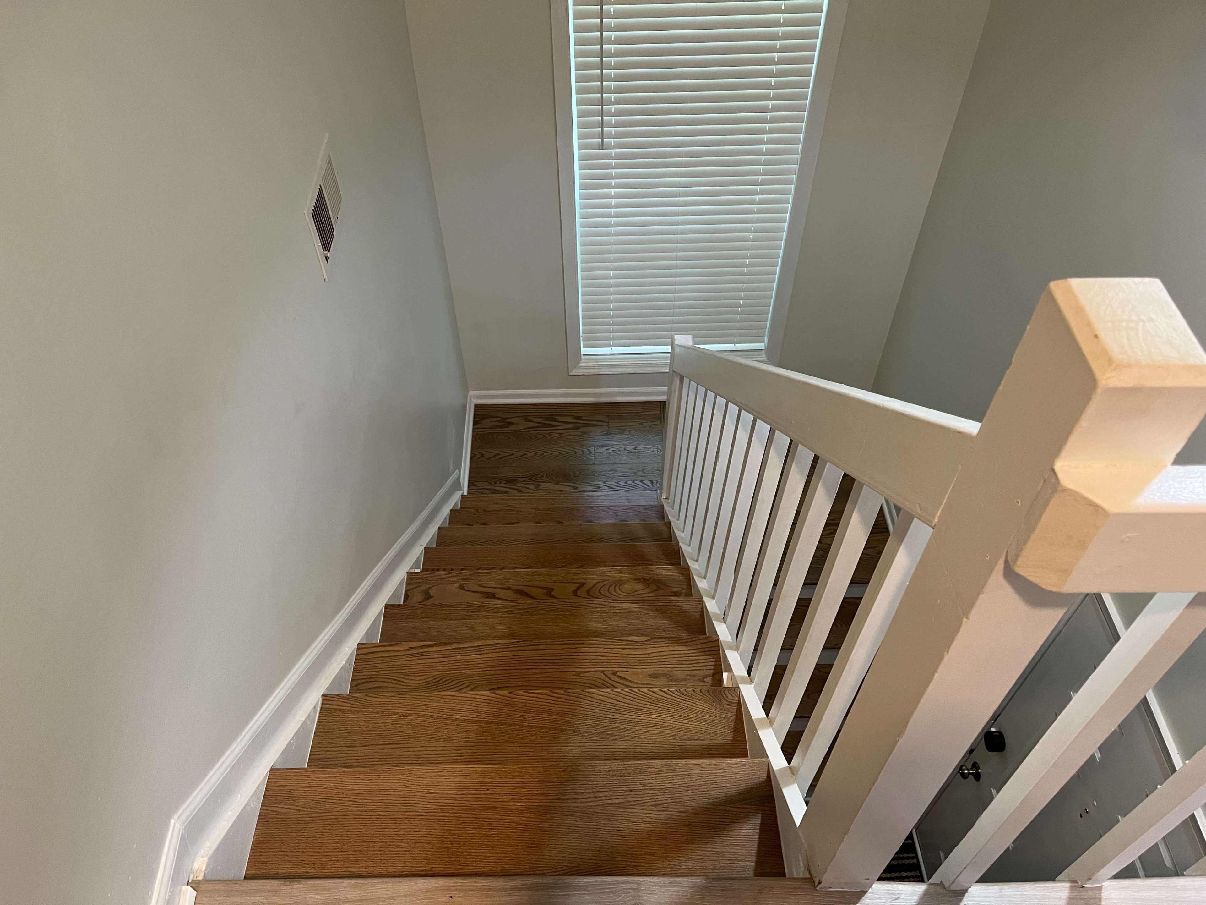 A wooden staircase leading down to a room with a window partially covered by blinds.
