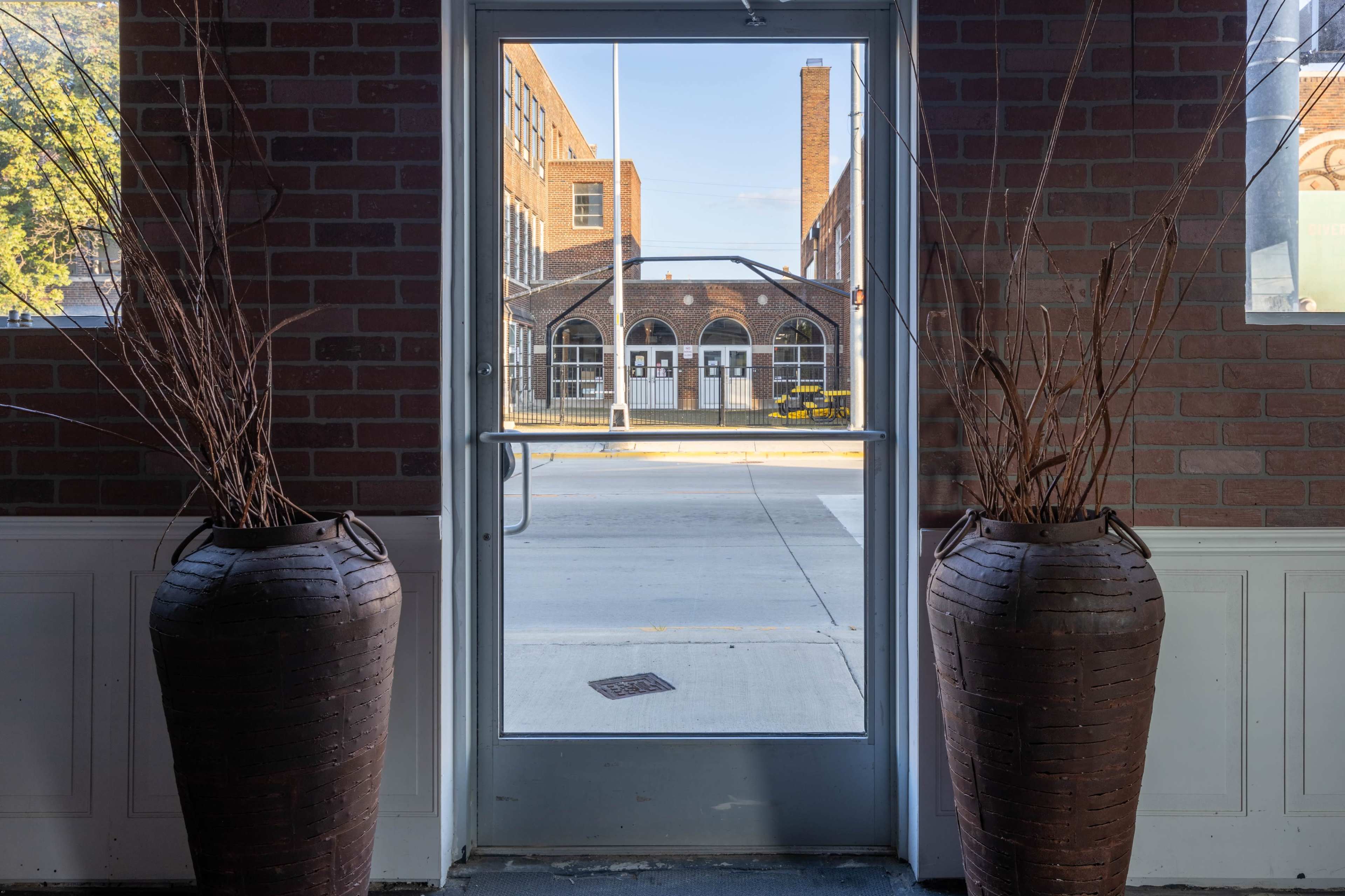 A view through a doorway framed by two large pots, revealing a brick building across a street.