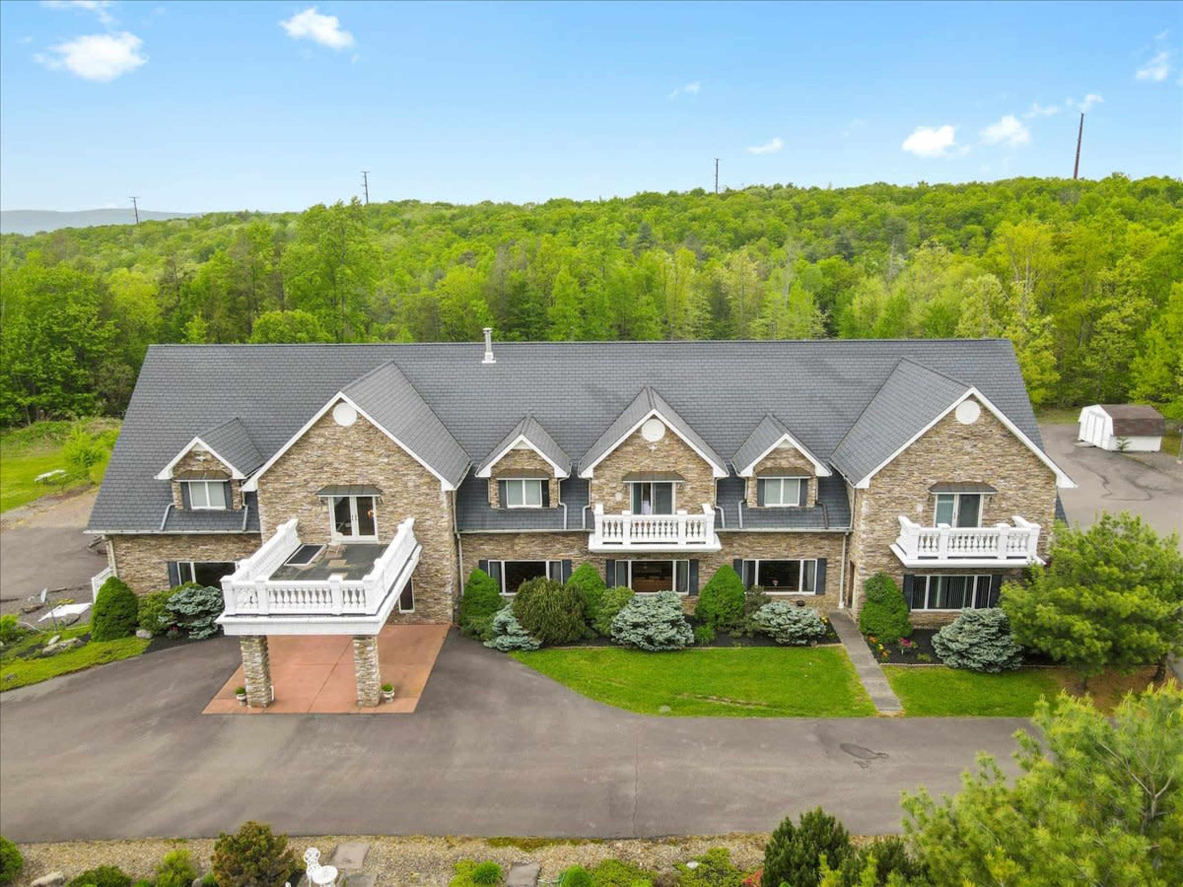 A large, stone-faced building with multiple sections and balconies, surrounded by landscaped greenery and a paved driveway.