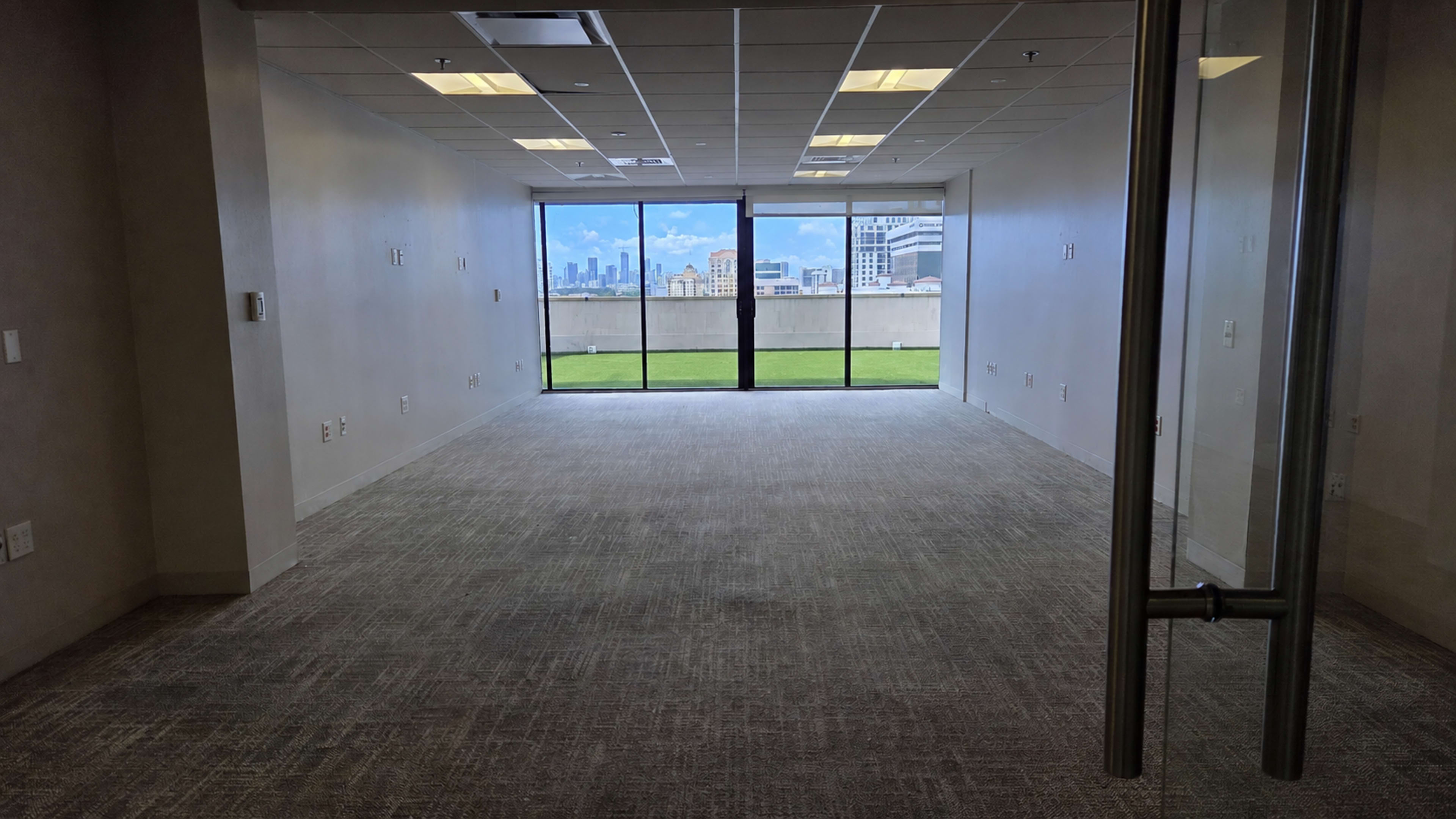 The image shows an empty office space with large windows overlooking a city skyline.
