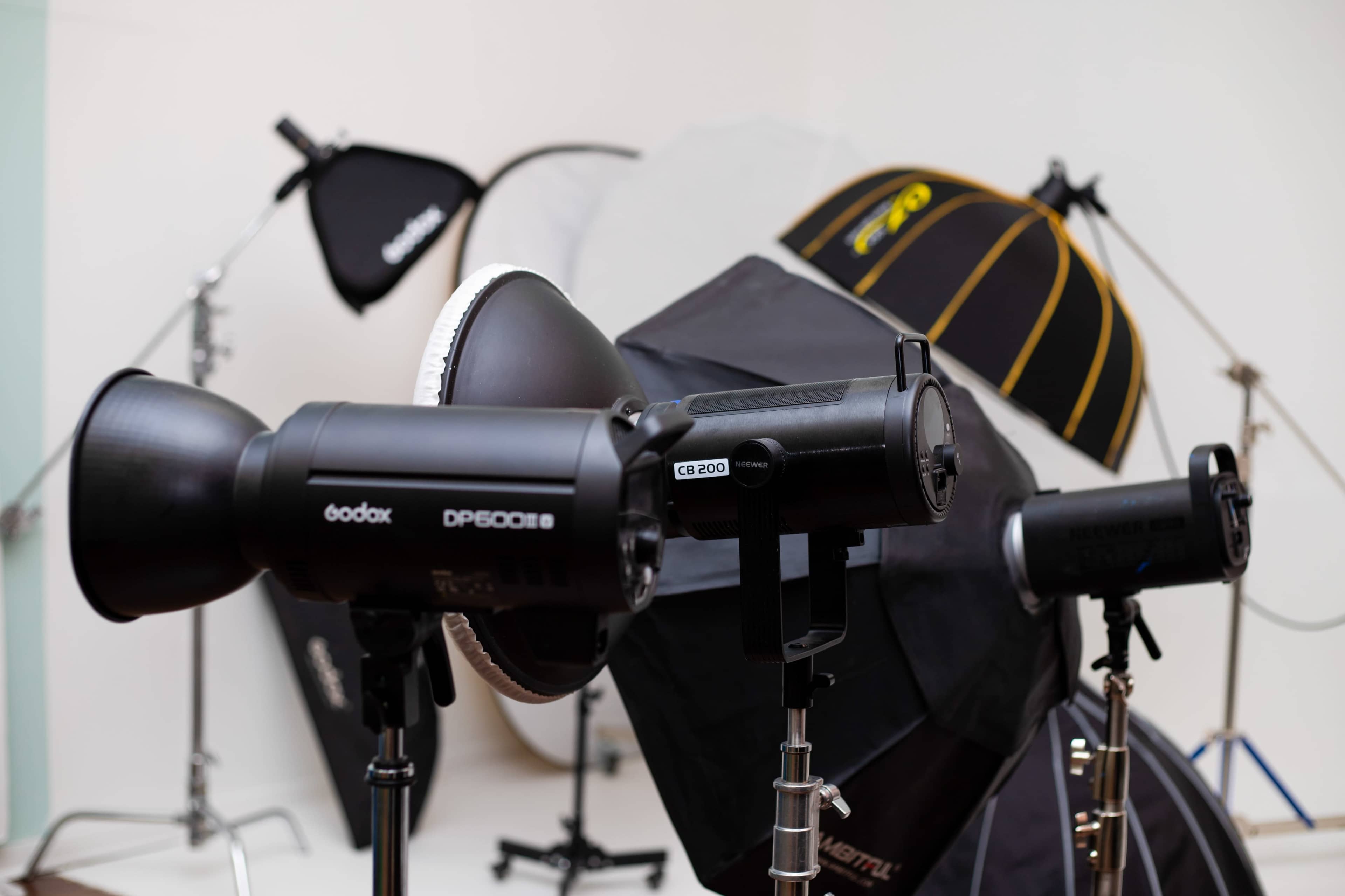 The image shows a photography studio with various lighting equipment, including softboxes and studio flash units set on tripods.