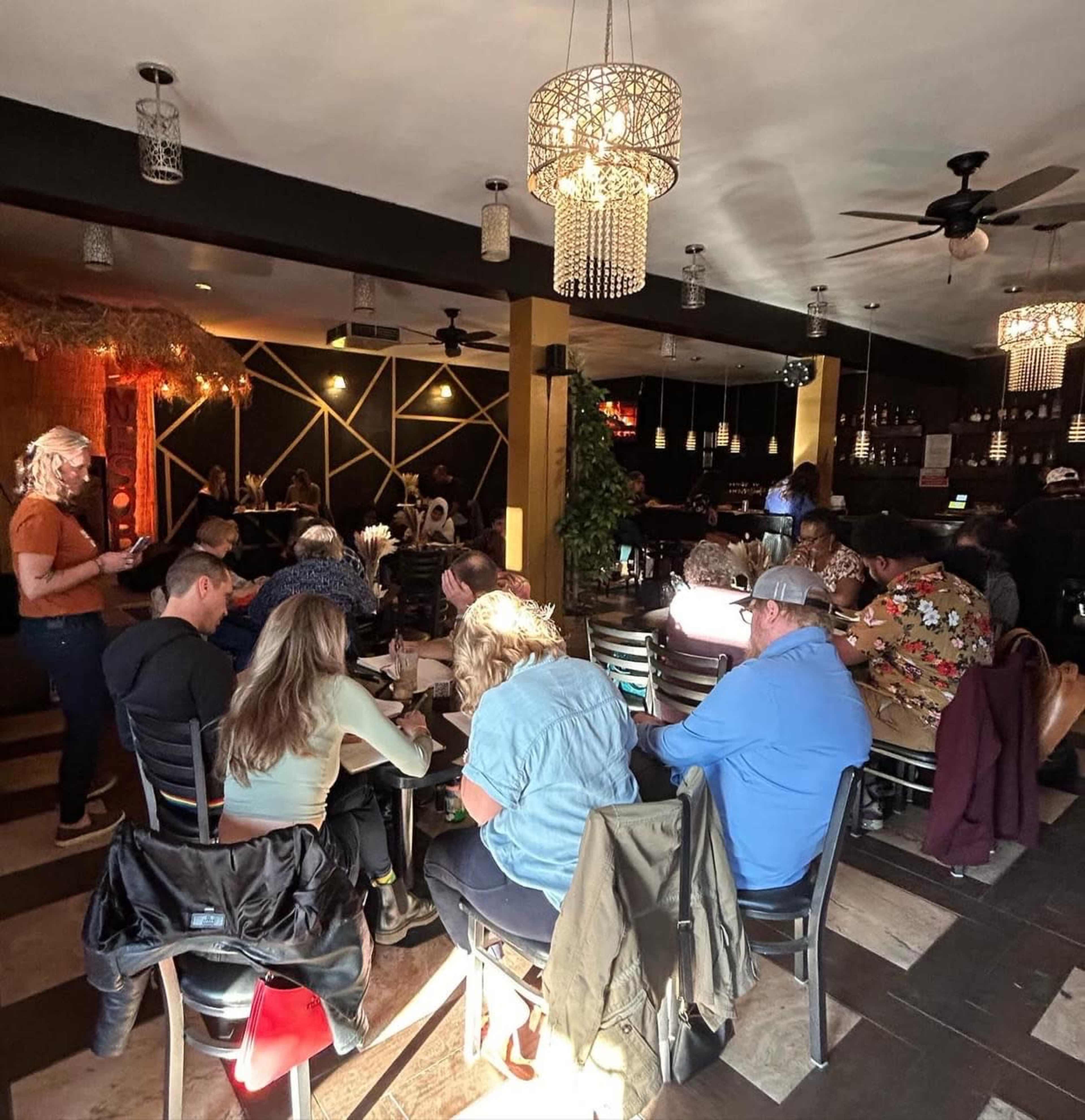 A dimly lit restaurant filled with diners seated at tables, some engaged in conversation while others focus on their meals.