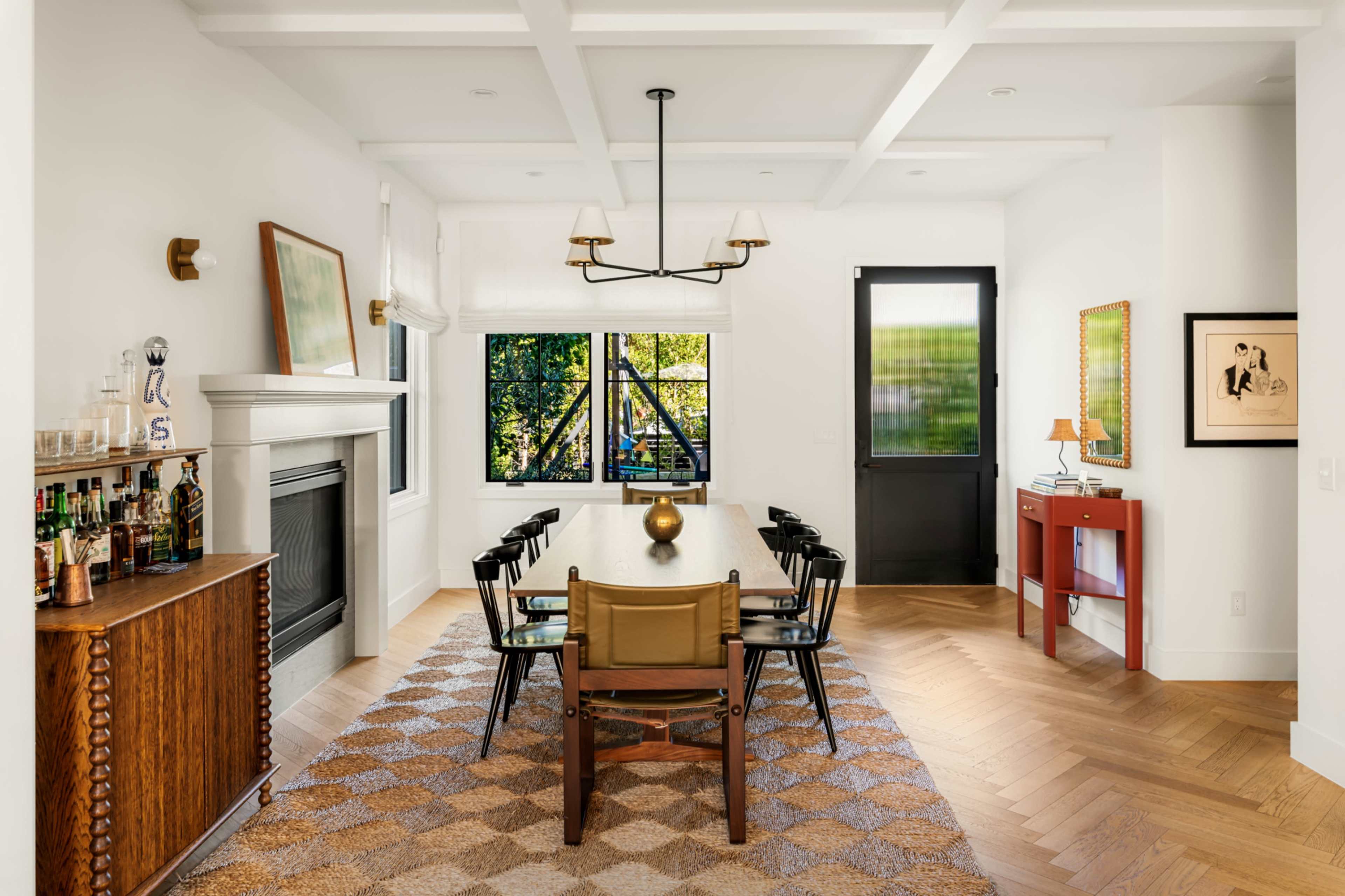 A spacious dining room features a long wooden table surrounded by black chairs, with a large window and a cozy fireplace in the background.