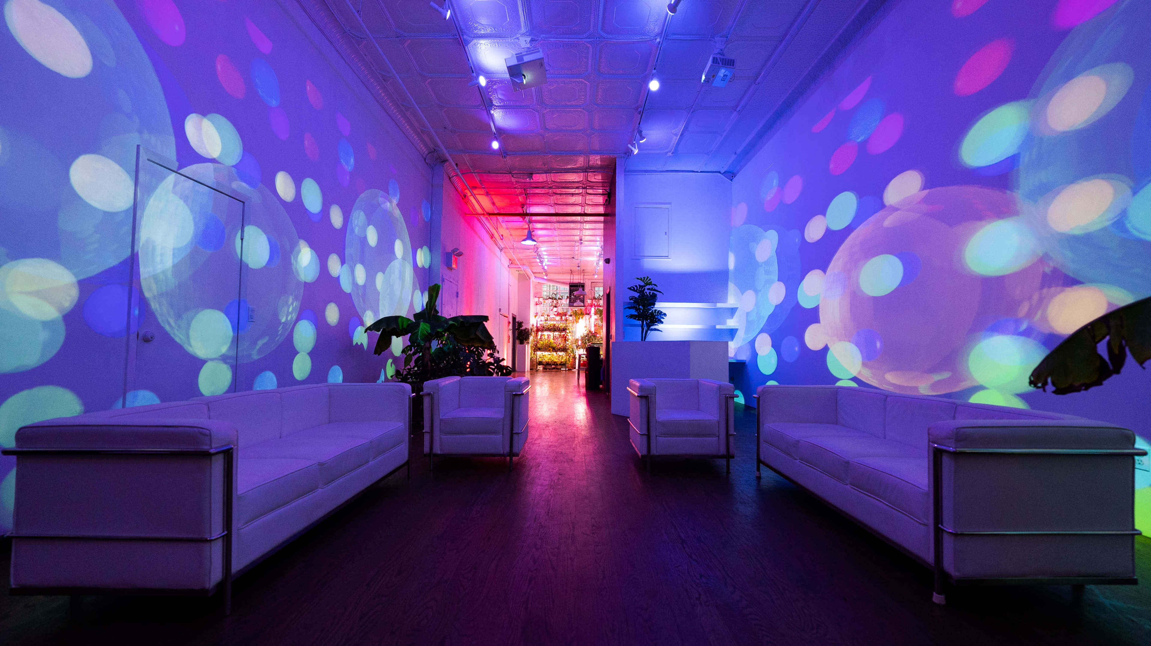 The room features white sofas arranged in a symmetrical layout, with colorful projections of circles illuminating the walls.