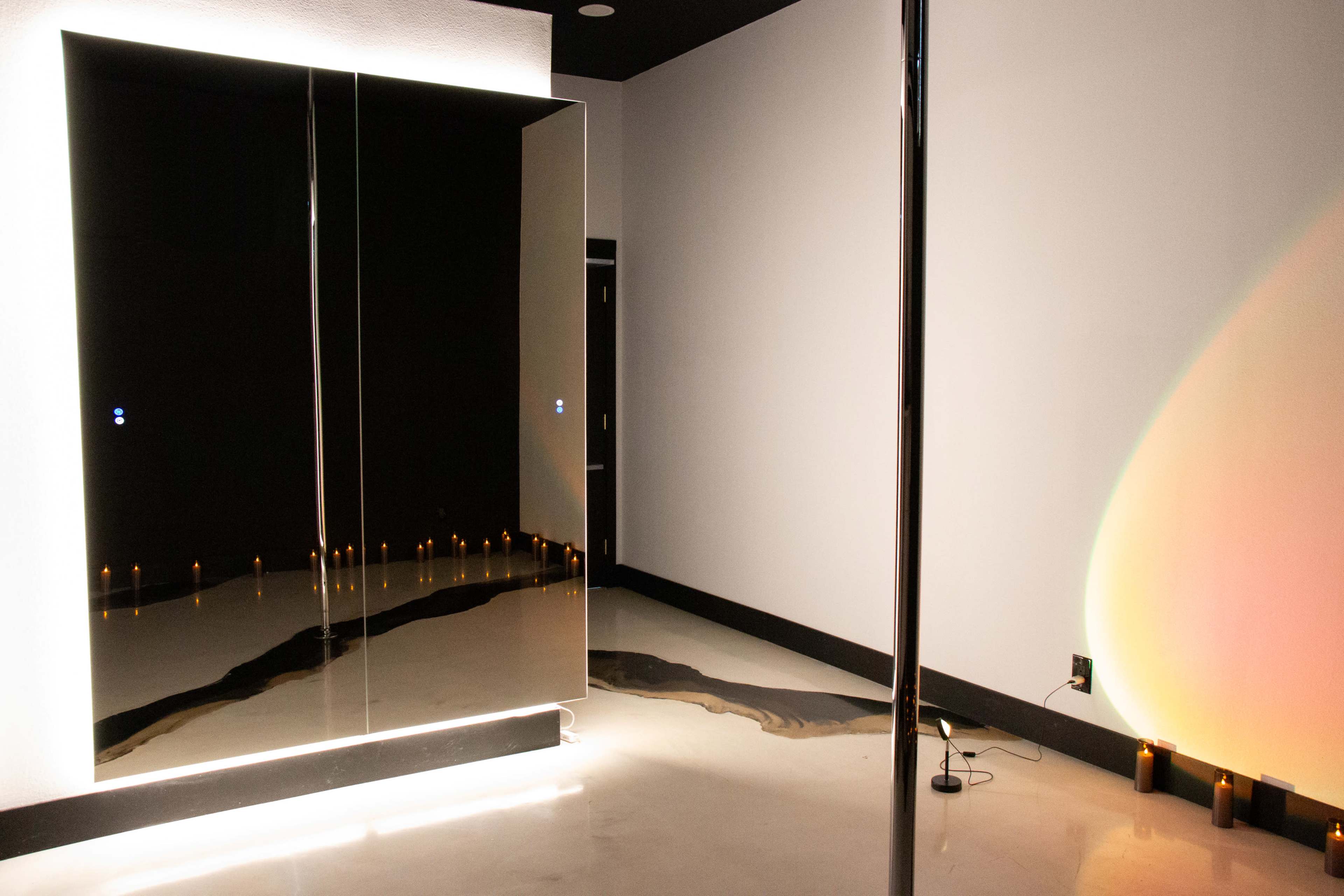 The image shows a dimly lit room with a large mirror and a polished floor, featuring a line of candles along one side.