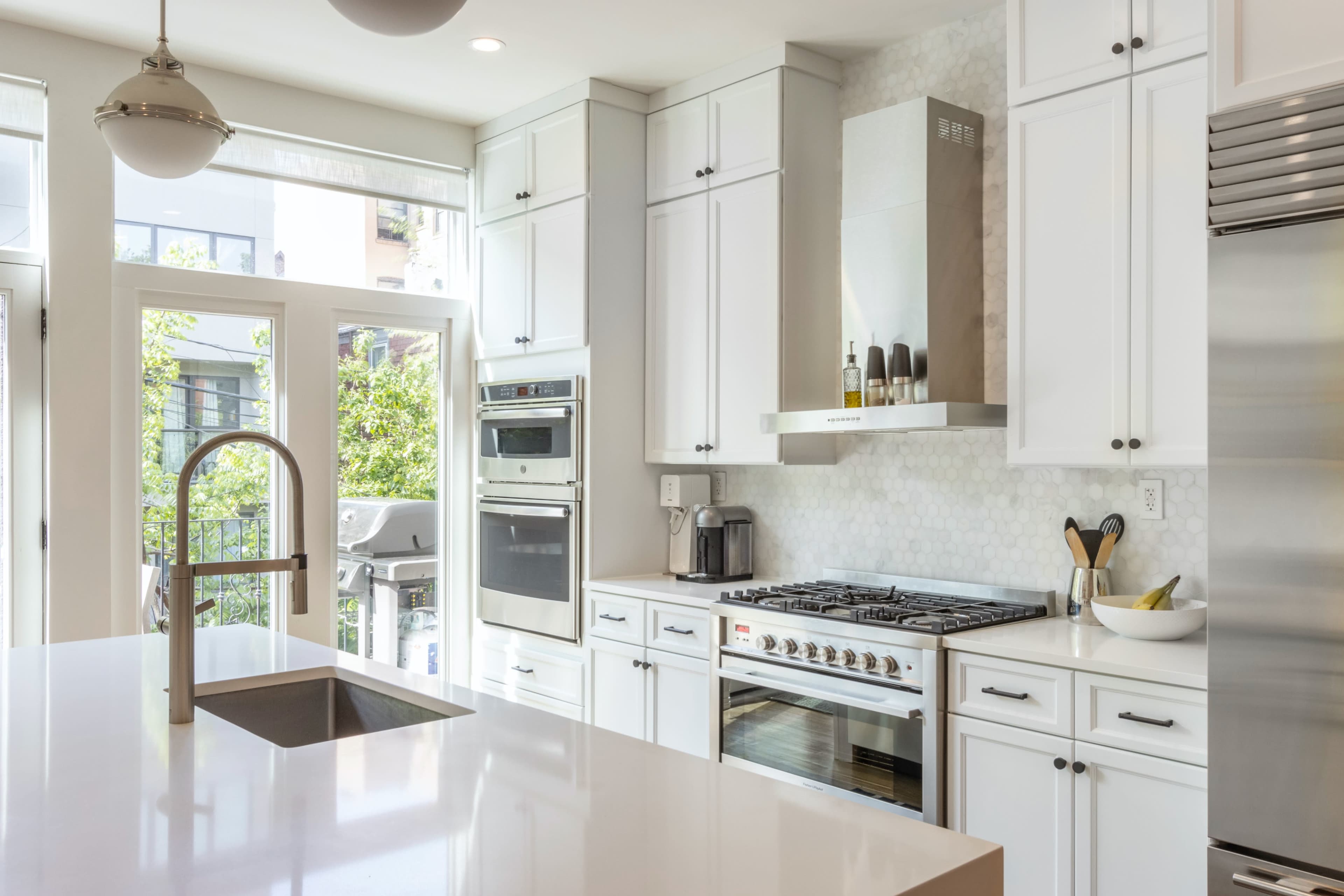 The image shows a modern kitchen with white cabinetry, stainless steel appliances, and a large island with a sink.