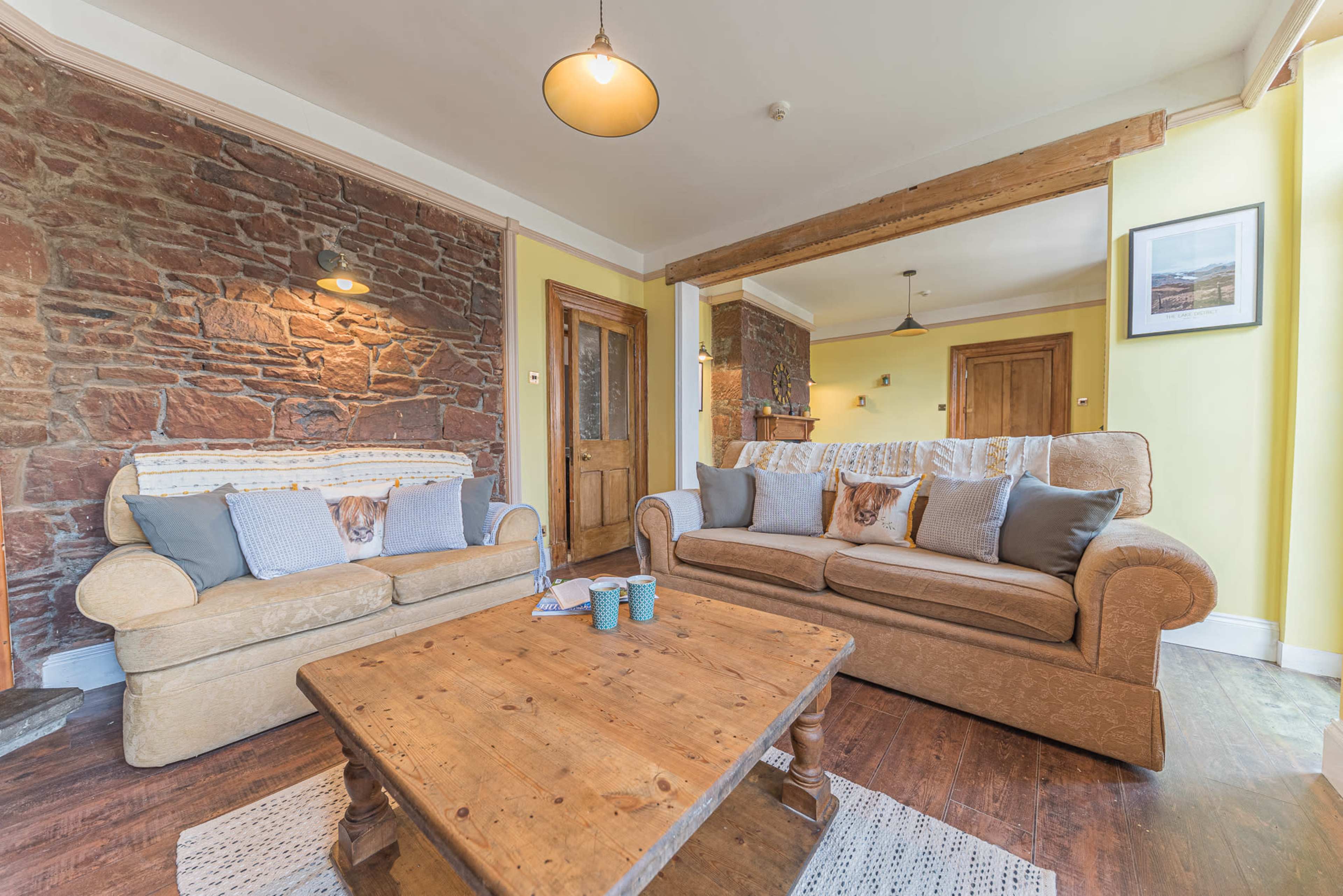 A living room with a combination of stone and yellow walls, featuring a beige sofa and a brown couch, with a wooden coffee table in the center.