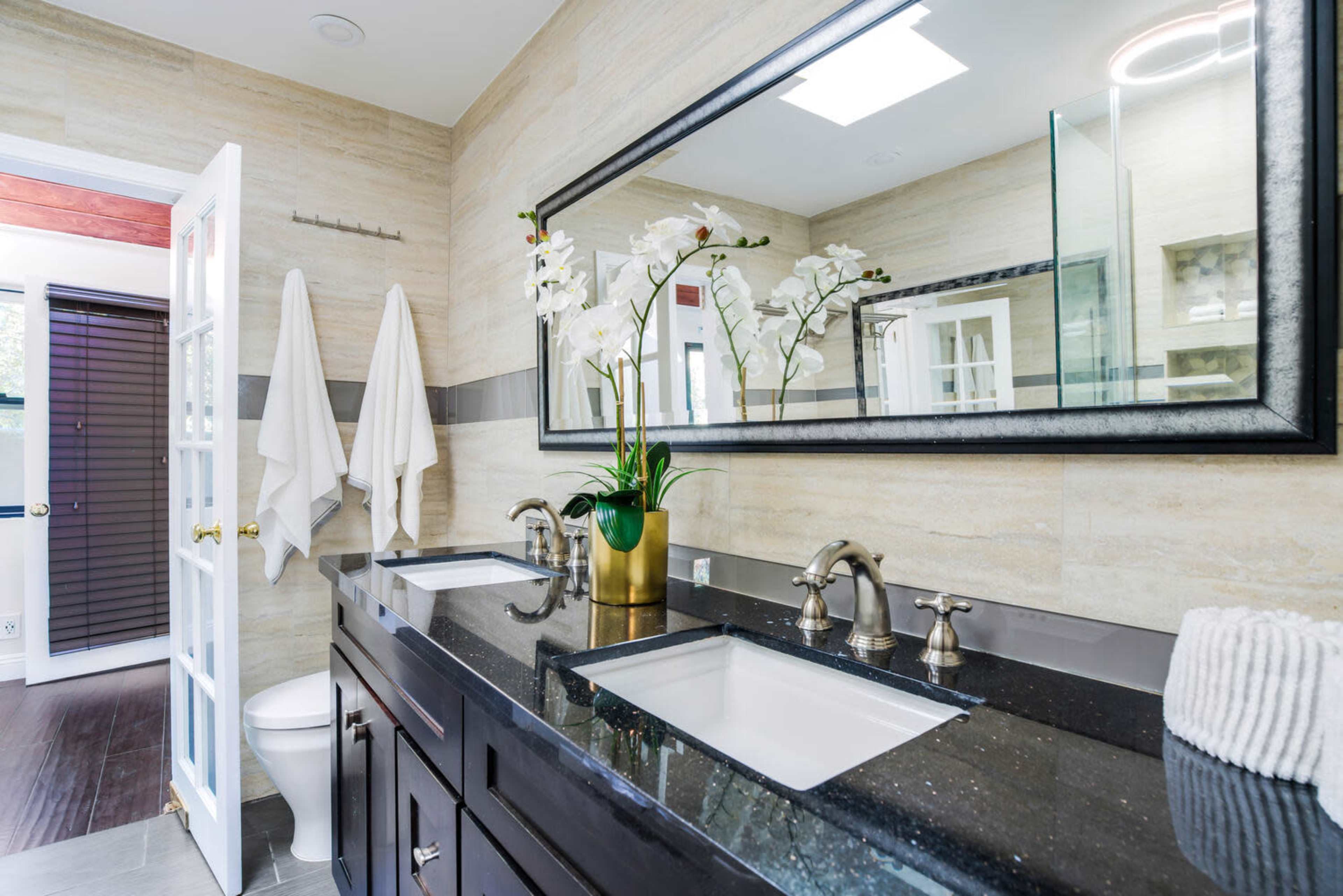 A modern bathroom with a double sink vanity, a large mirror, and decorative orchids.