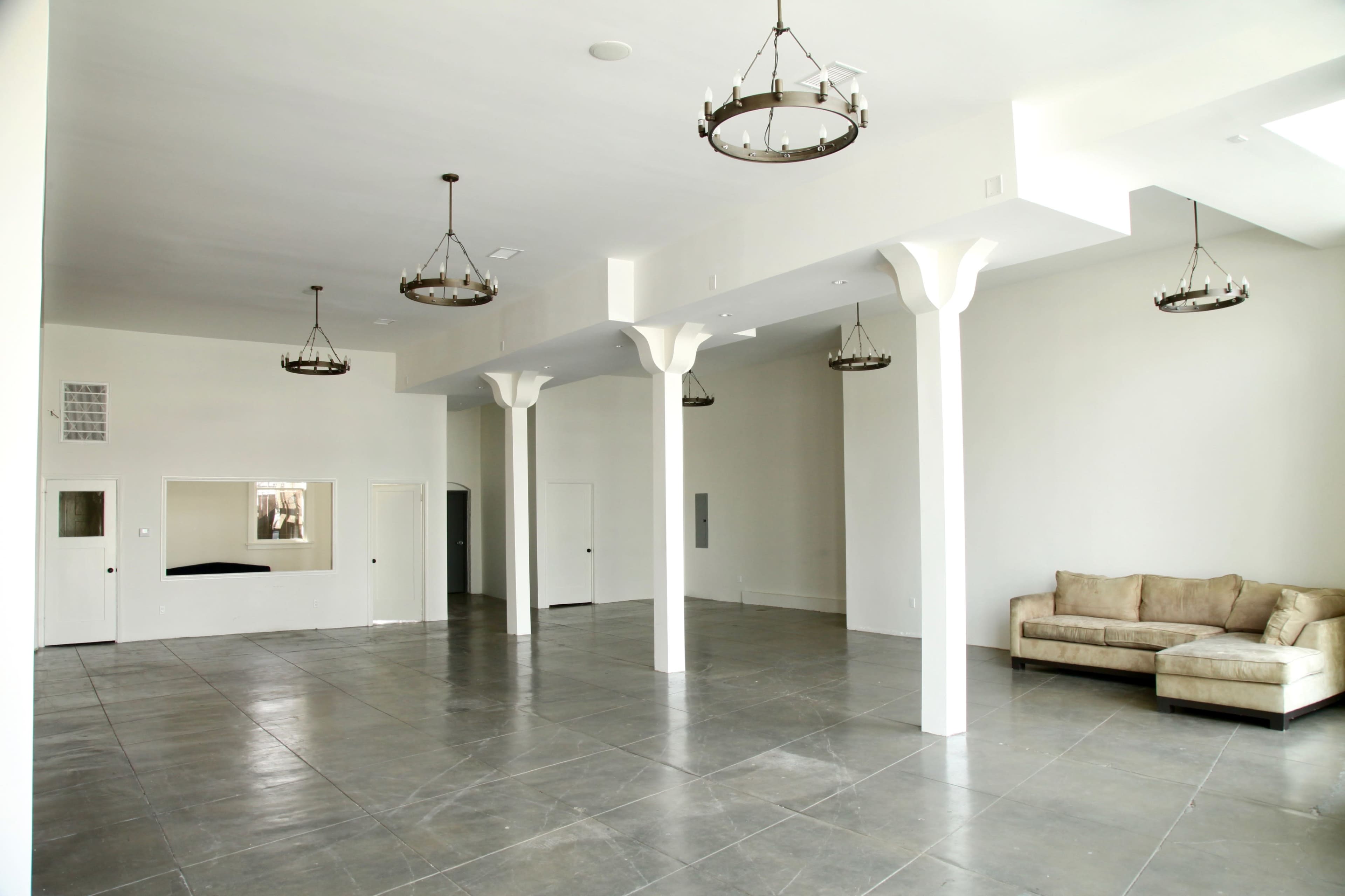 An open, empty interior space with concrete flooring, white walls, and several hanging light fixtures.