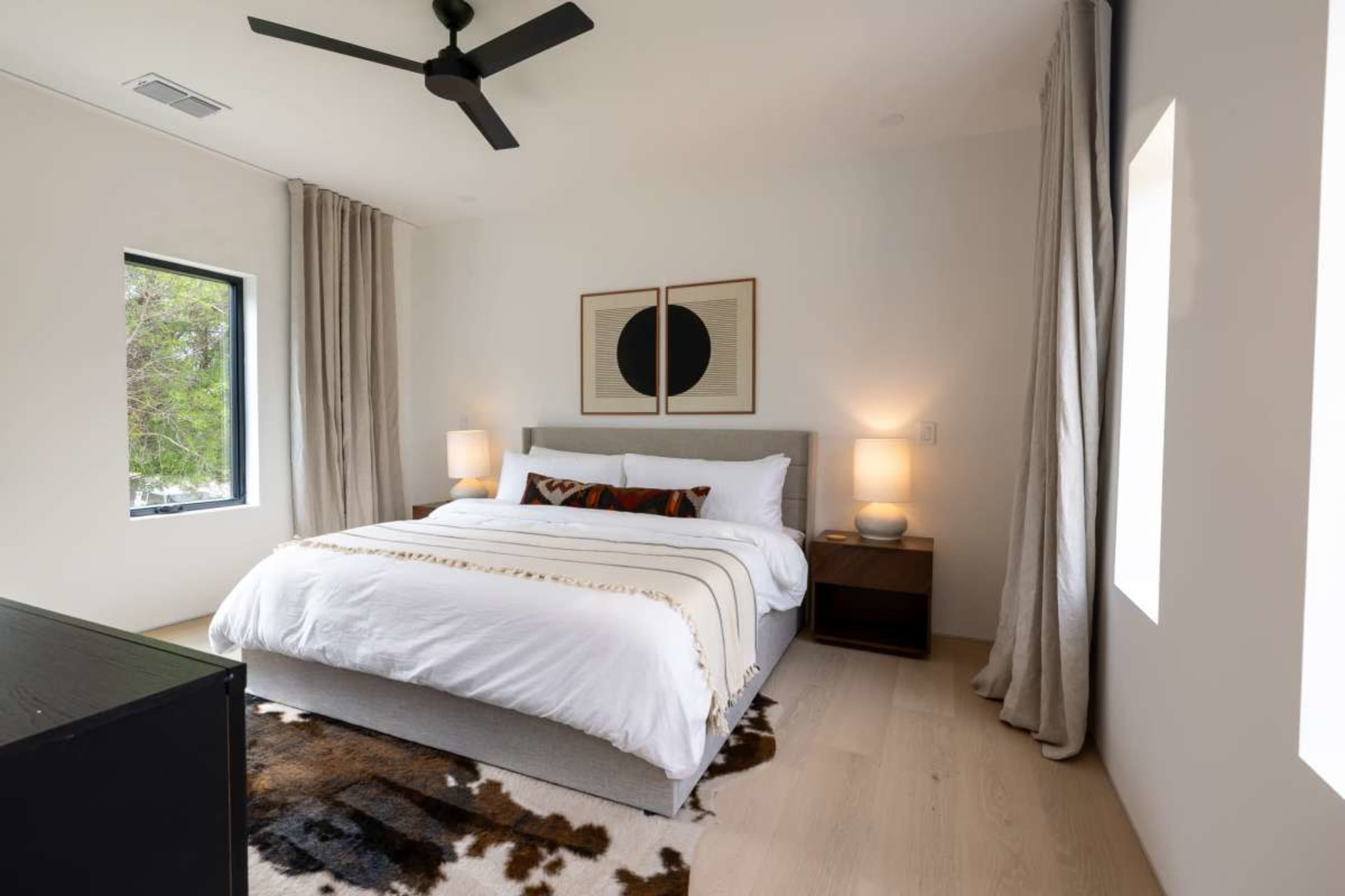 The room features a bed with white linens, two bedside lamps on wooden nightstands, and framed art hanging on the wall.