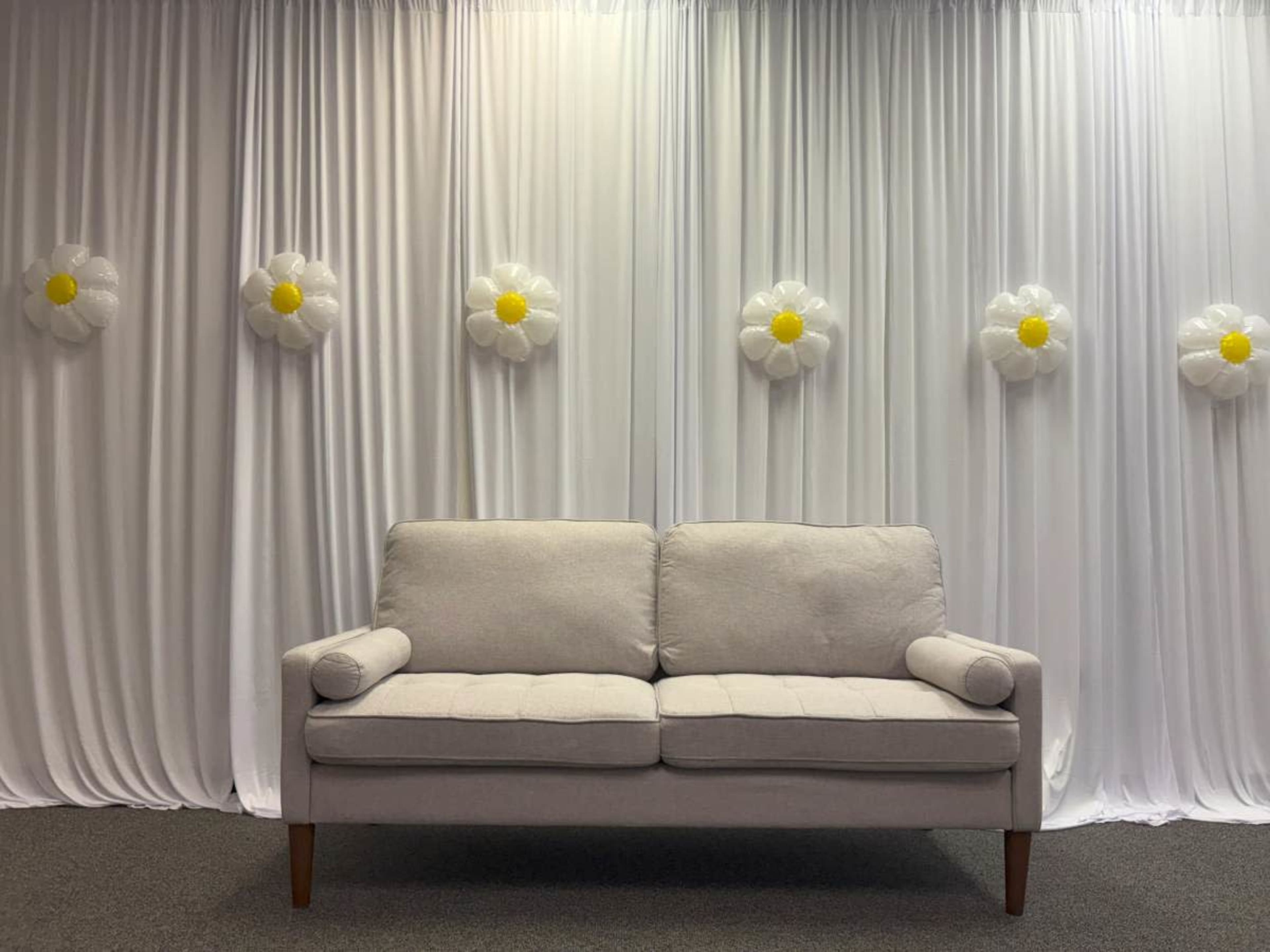 A plain beige couch is positioned in front of a white curtain adorned with large, flower-shaped decorations.