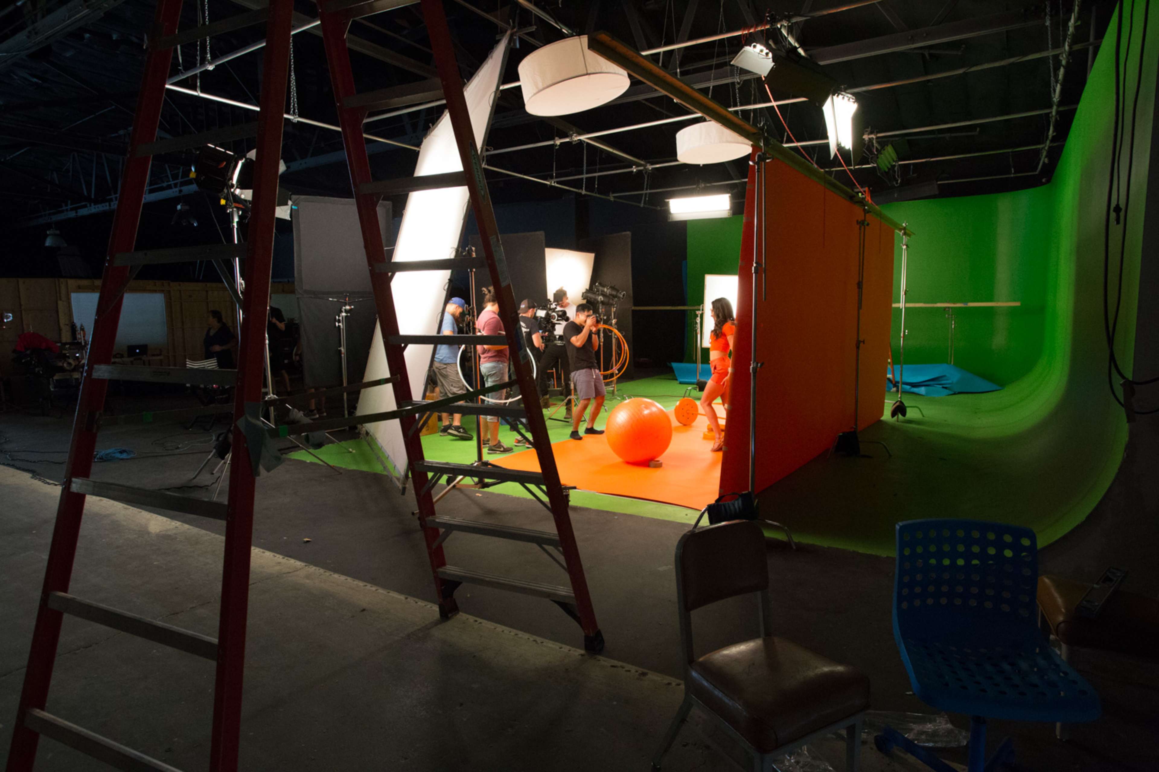 A film crew sets up a colorful scene inside a studio with various lighting equipment and a large green backdrop.