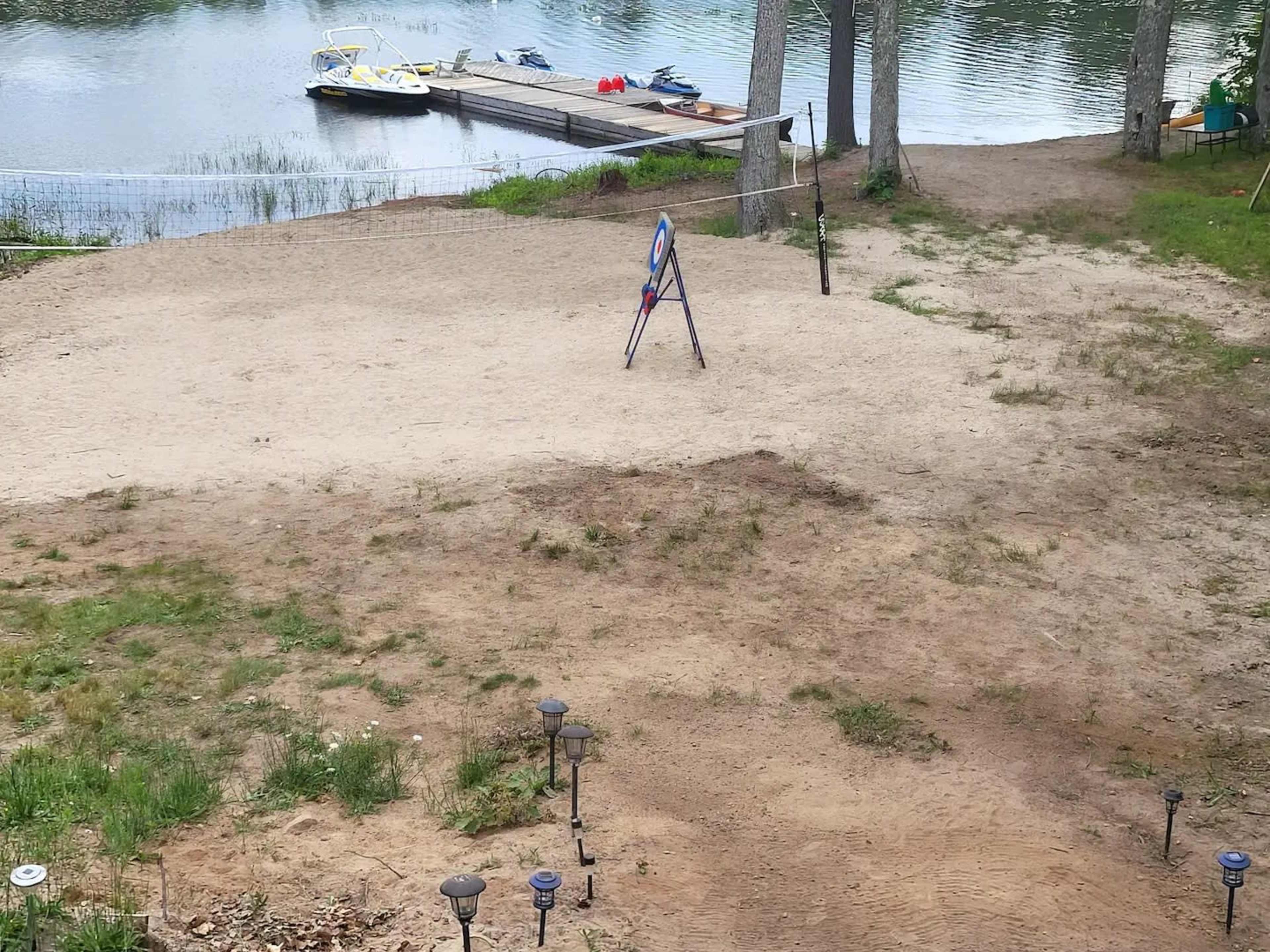 A sandy area near a calm body of water, with a dock and parked personal watercraft in the background.