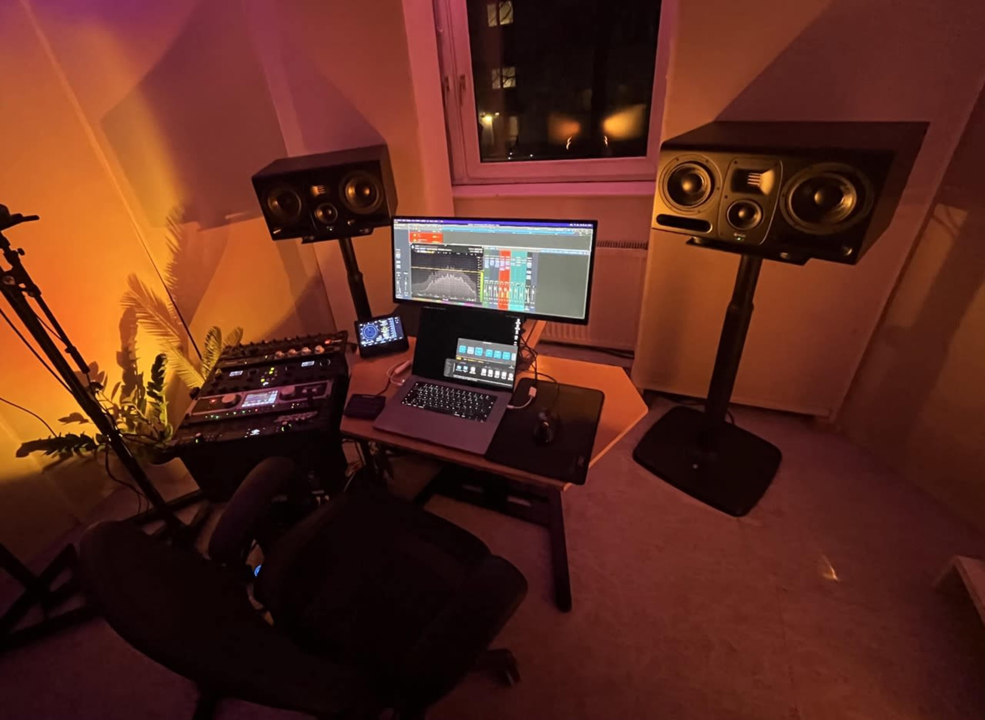 A music production setup features a computer monitor, audio interface, and two studio monitors in a room with low ambient lighting.