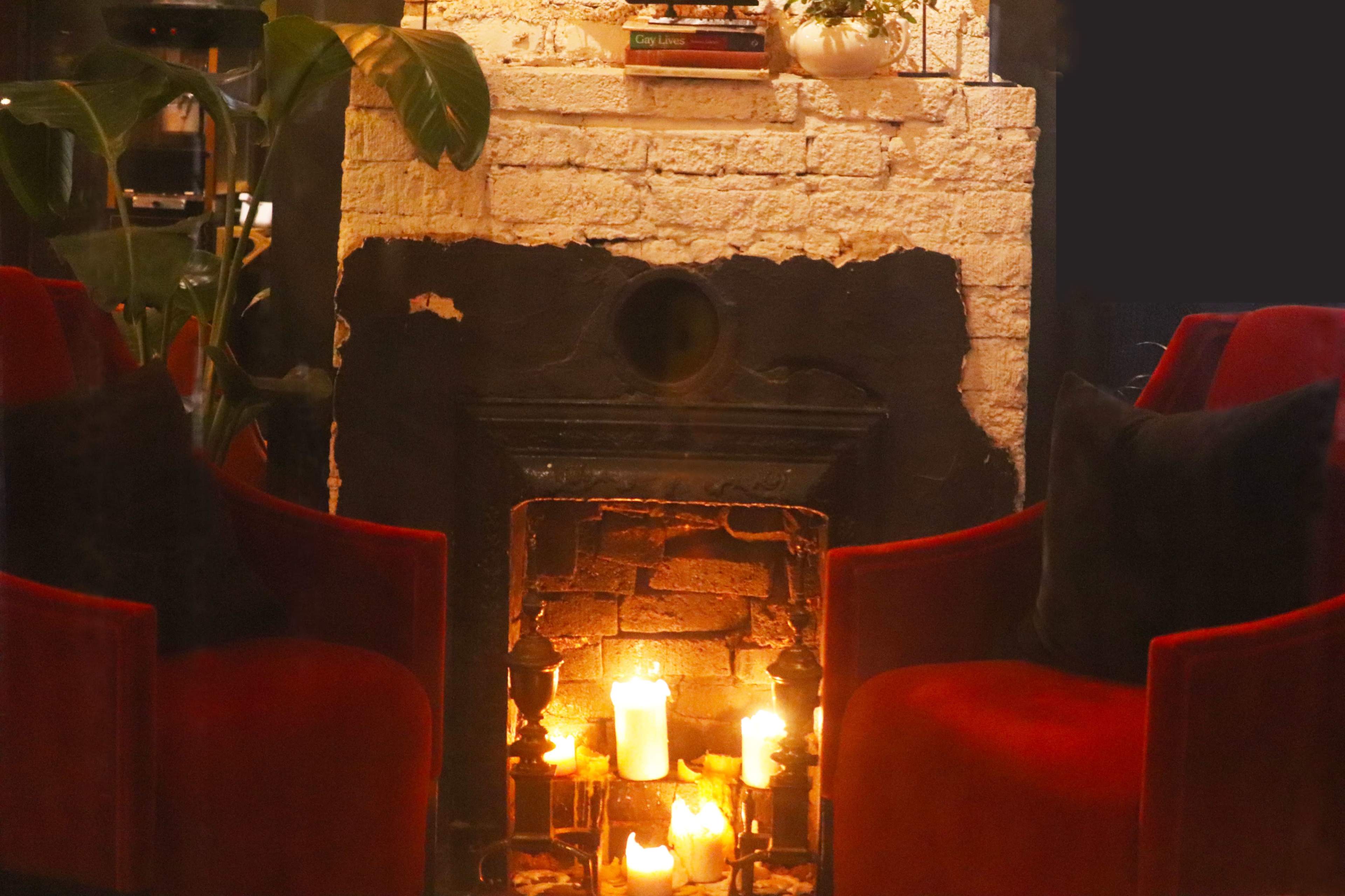 Two red armchairs sit near a brick fireplace adorned with several lit candles.