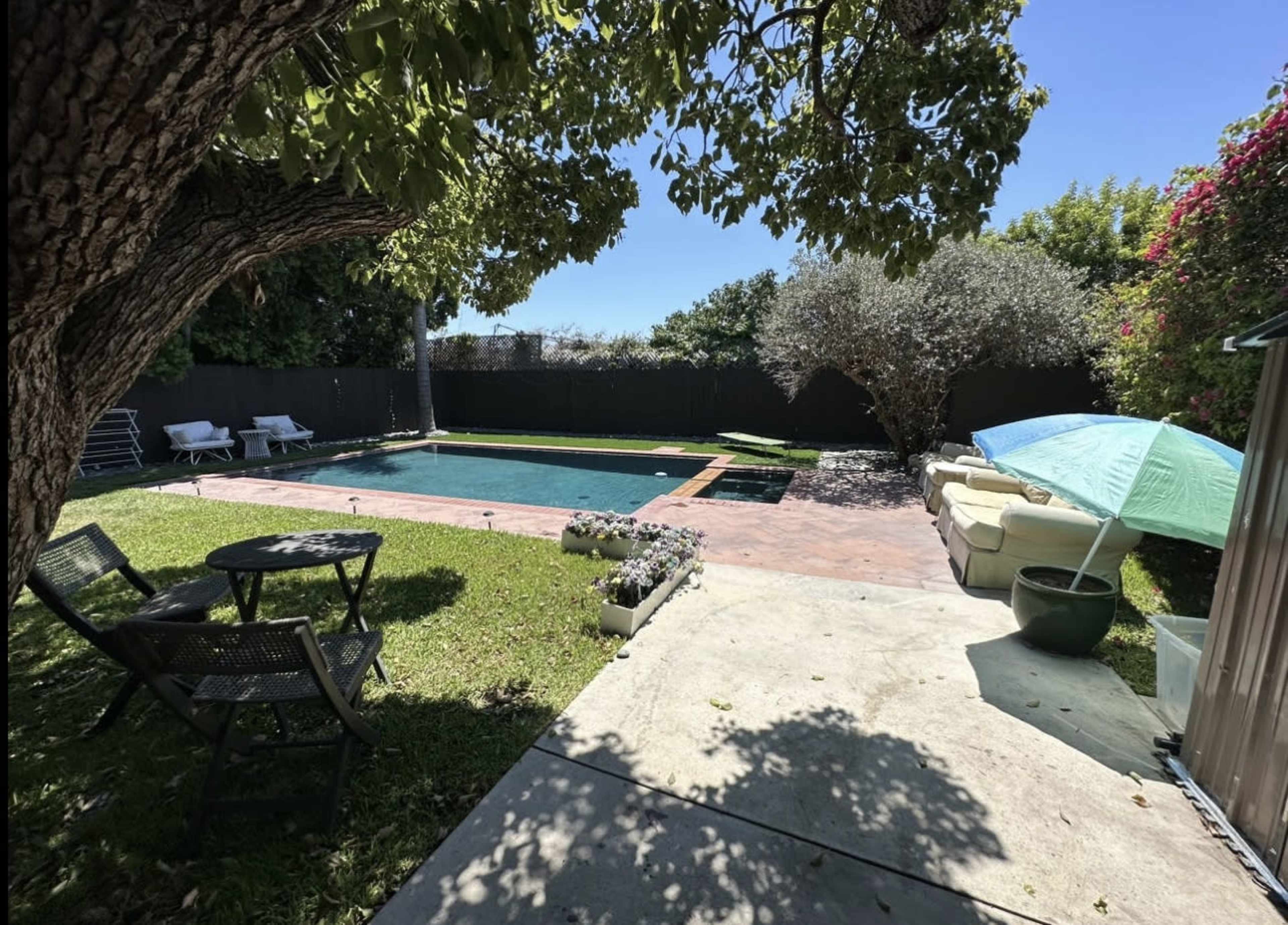 A backyard with a swimming pool, surrounded by greenery and outdoor seating areas.