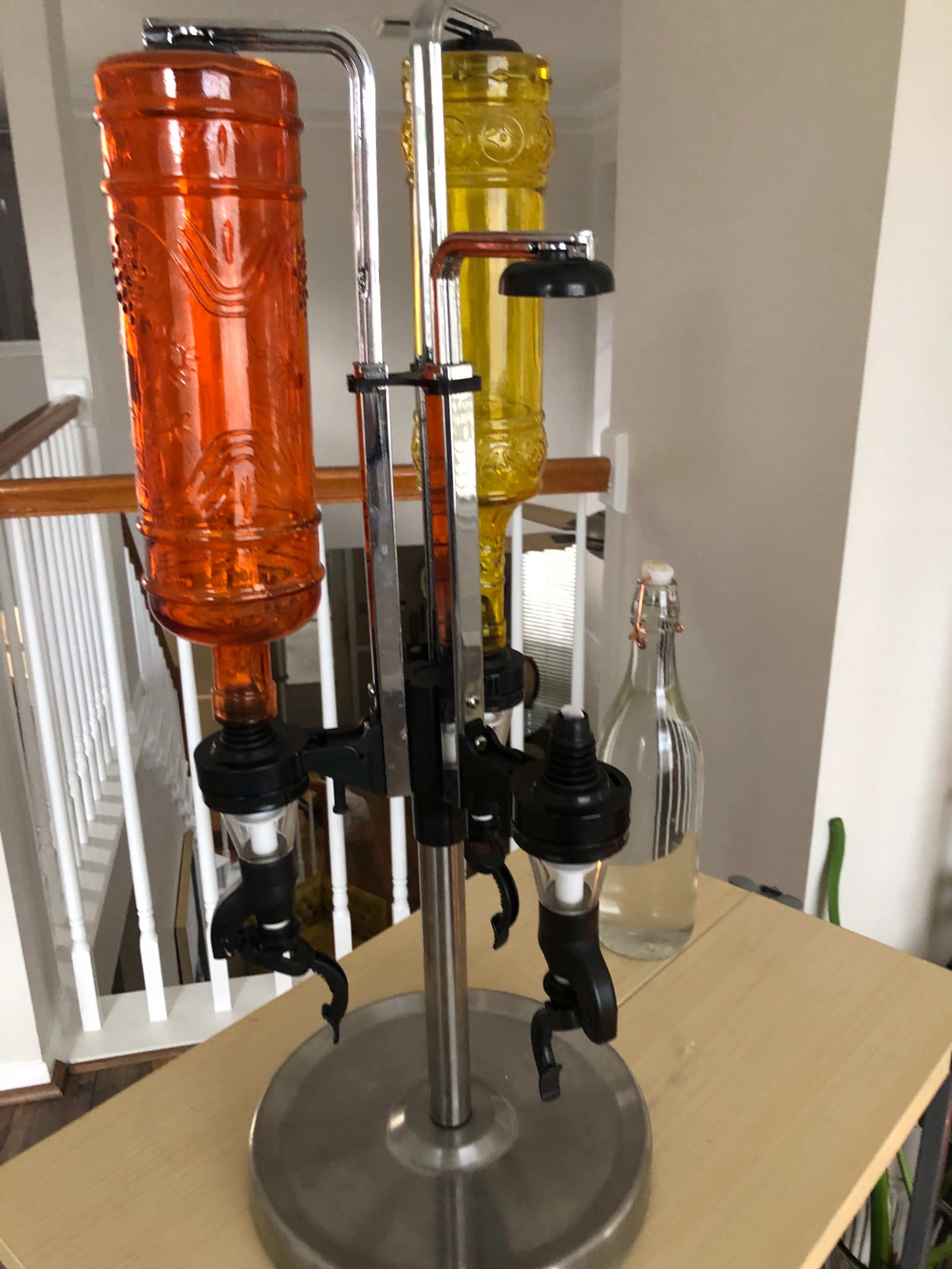 A drink dispenser with two large, brightly colored plastic containers mounted on a metal stand, each featuring a spout at the bottom for pouring.