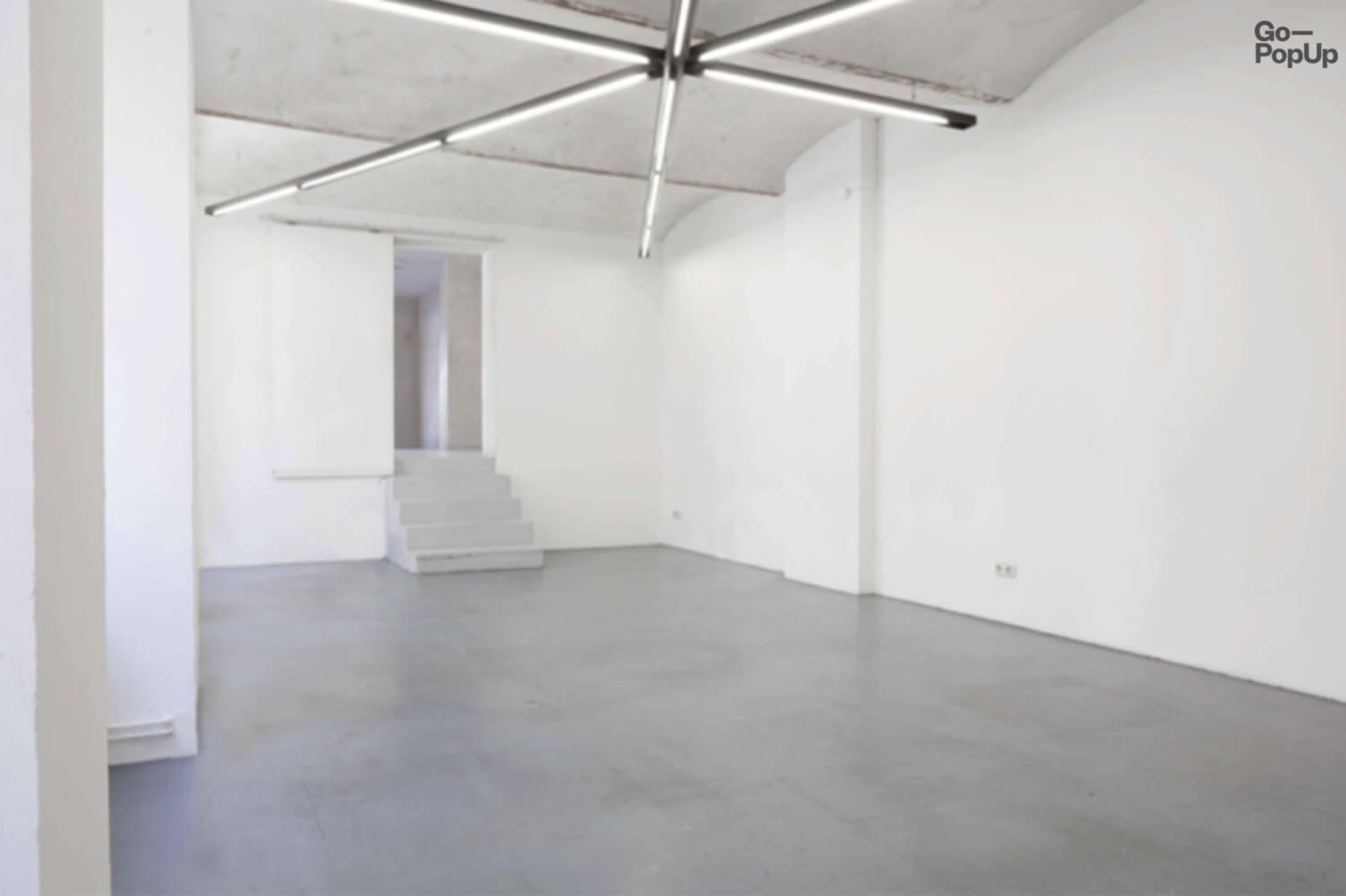 A minimalist, empty room with white walls, a concrete floor, and a staircase leading to an upper level.