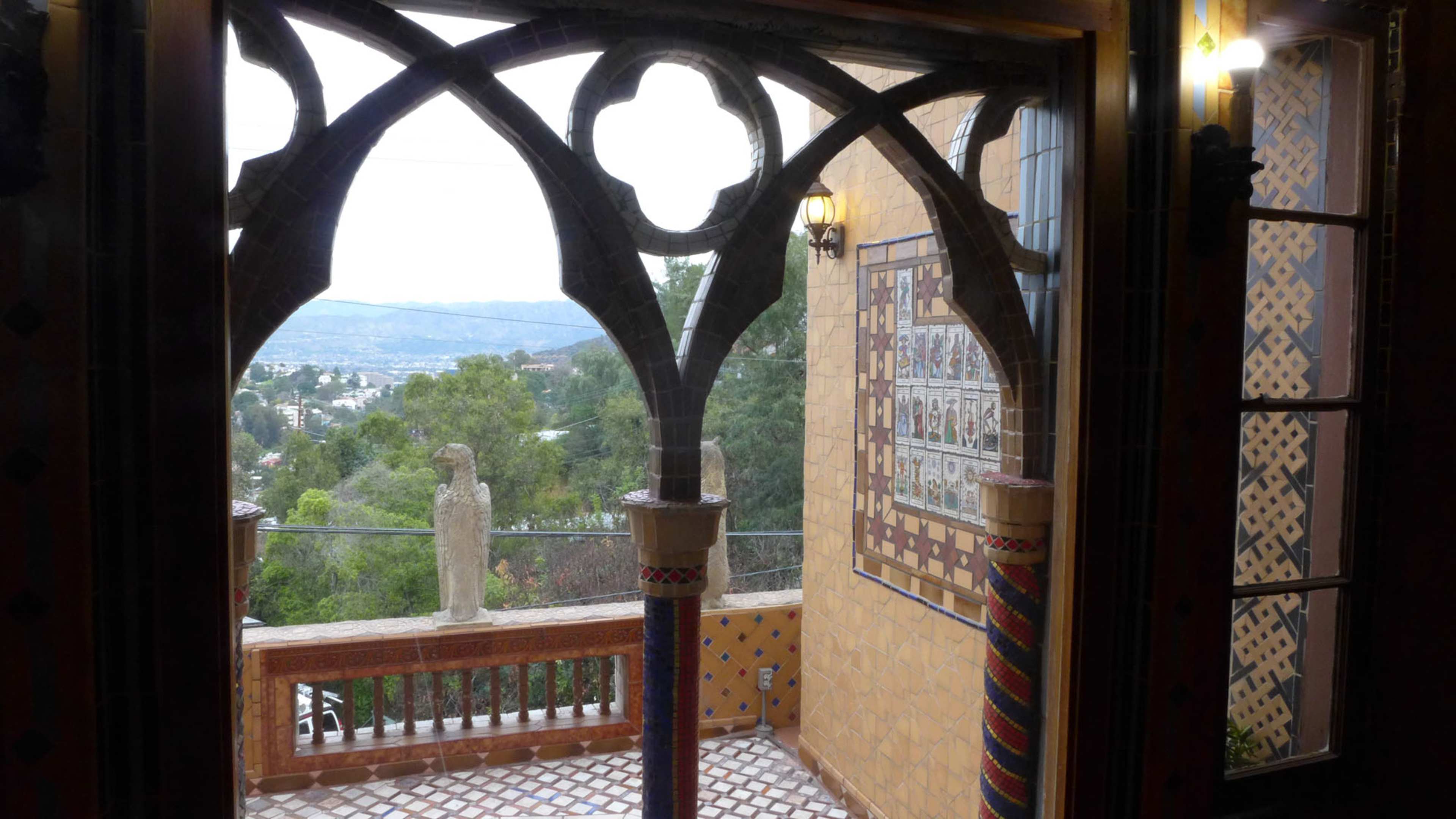 An ornate window arch framing a view of a landscape with trees and distant hills.