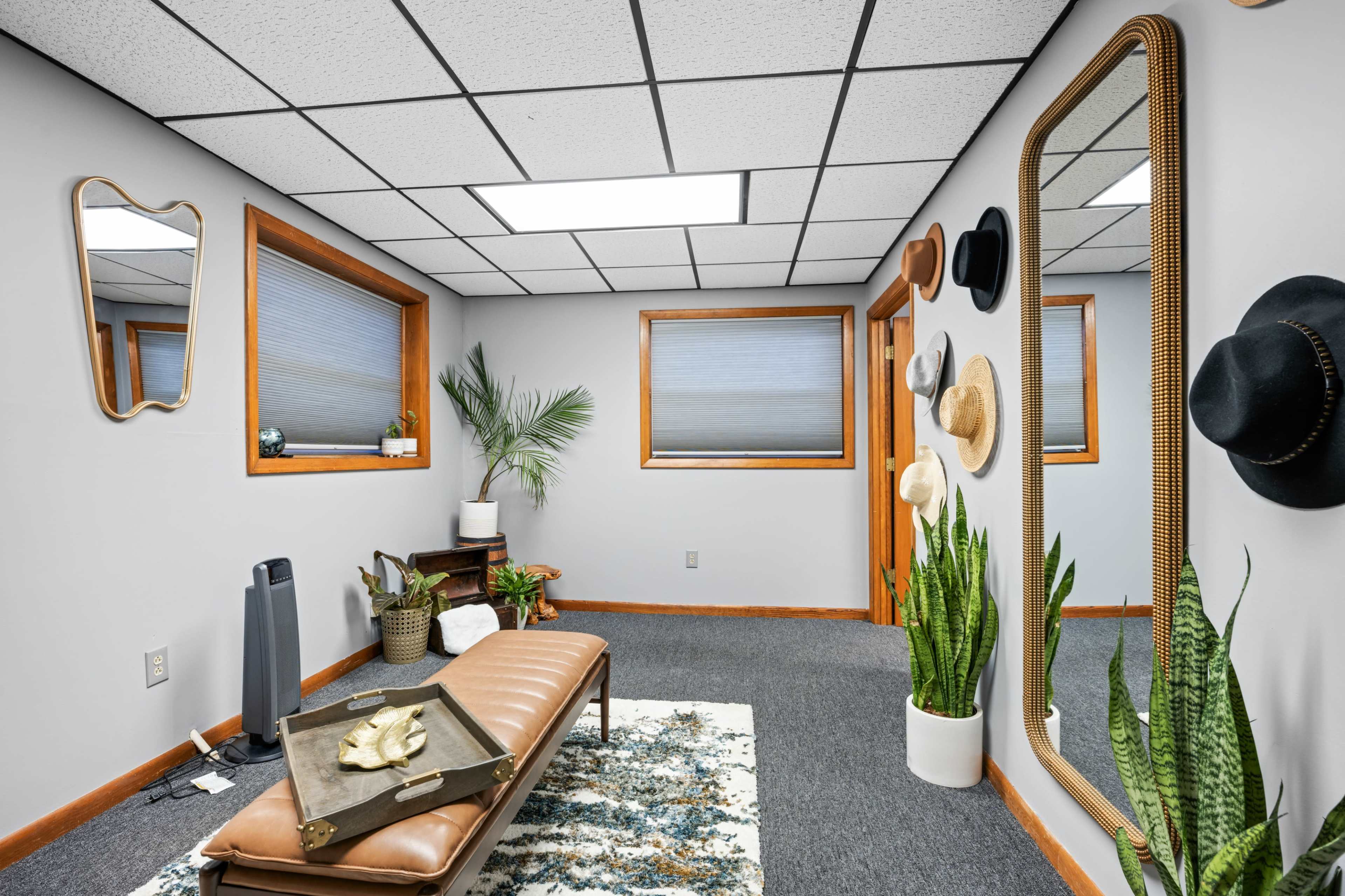 A bright room featuring a bench, potted plants, a large mirror, and hats displayed on the walls.