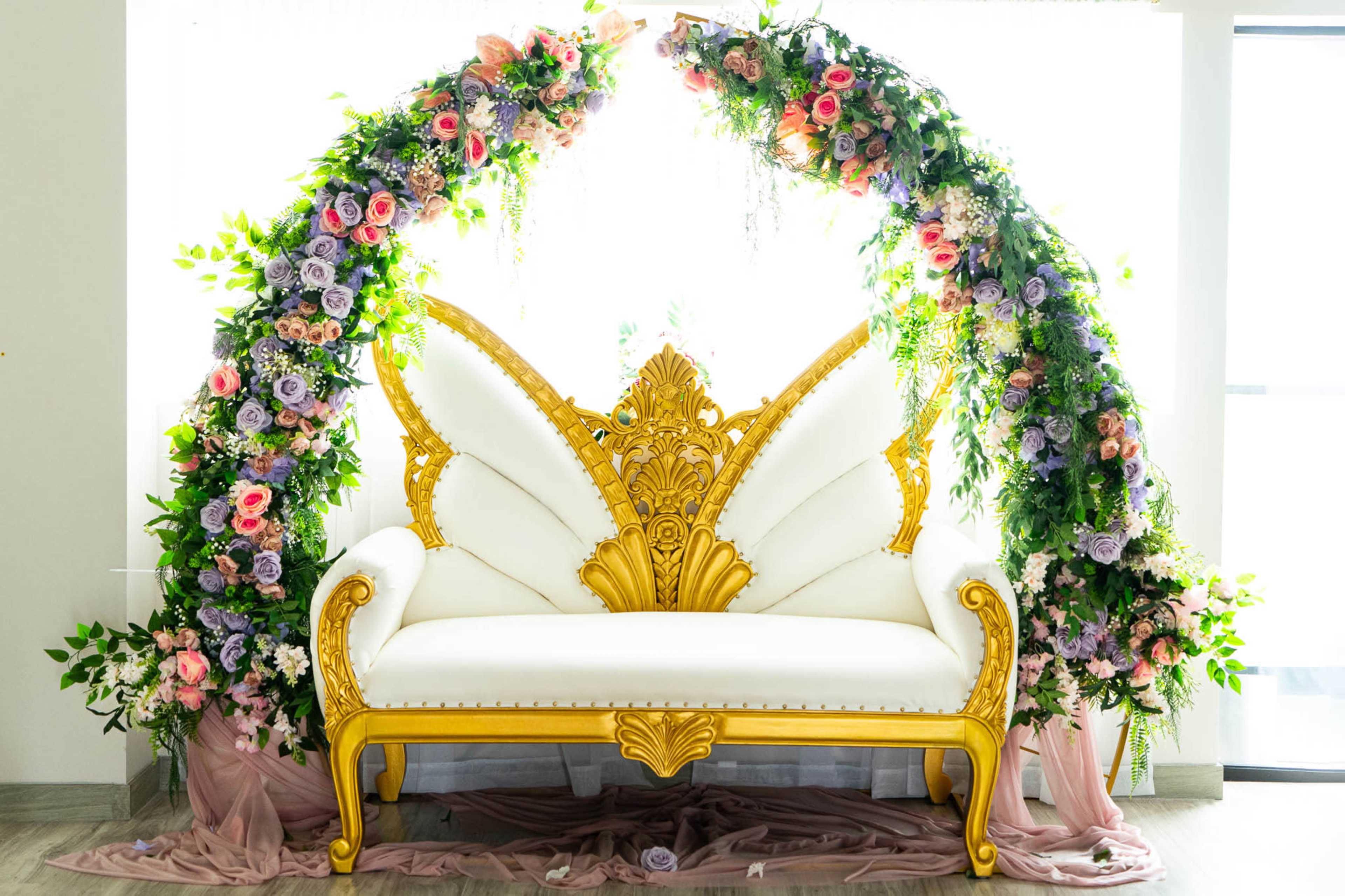 A gold-accented white sofa with a butterfly design is surrounded by an arch of colorful flowers.